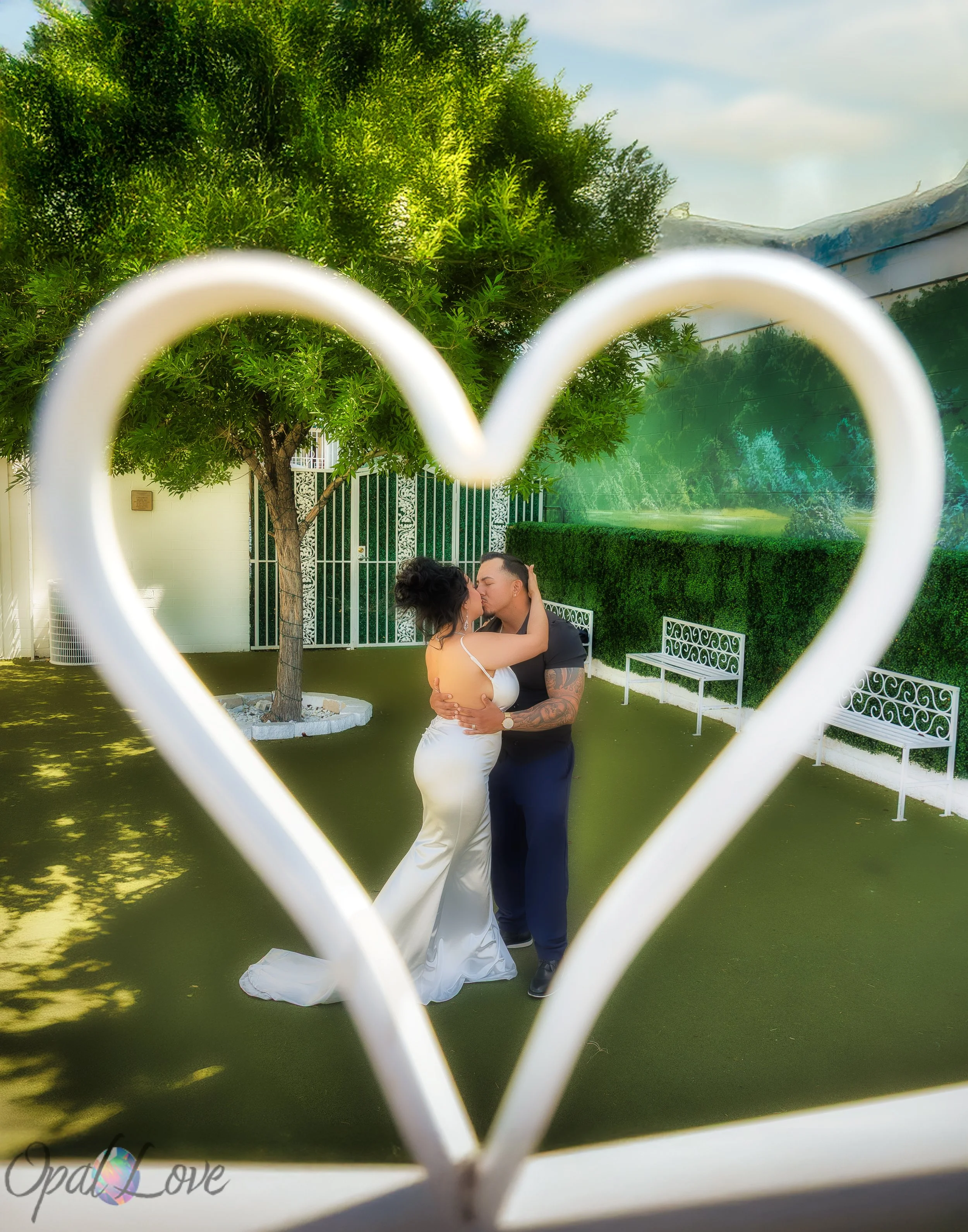 Couple kissing in a garden courtyard, framed by a white heart-shaped gate