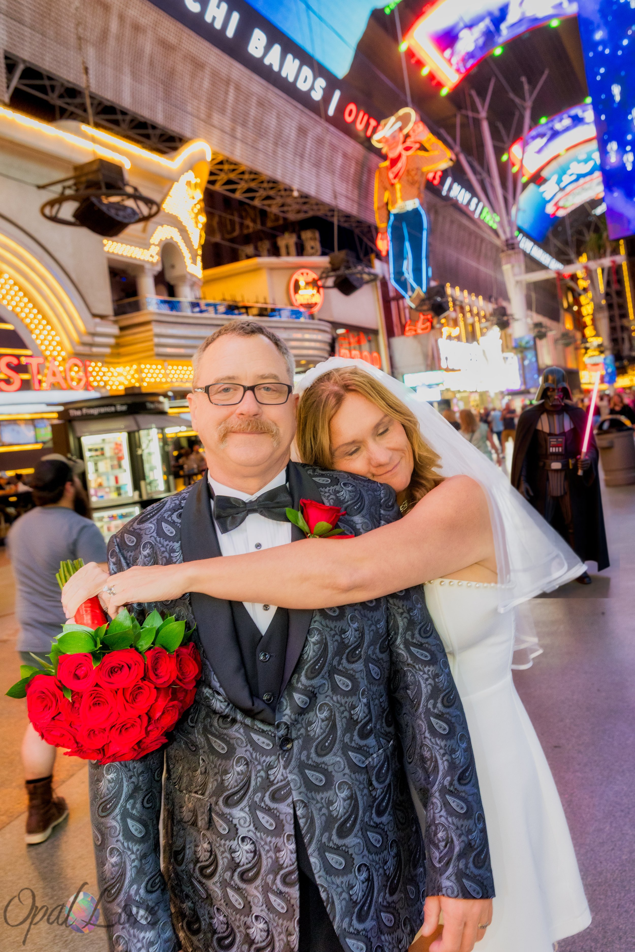 Newly married couple hugging beneath the neon lights on Fremont Street in Las Vegas.