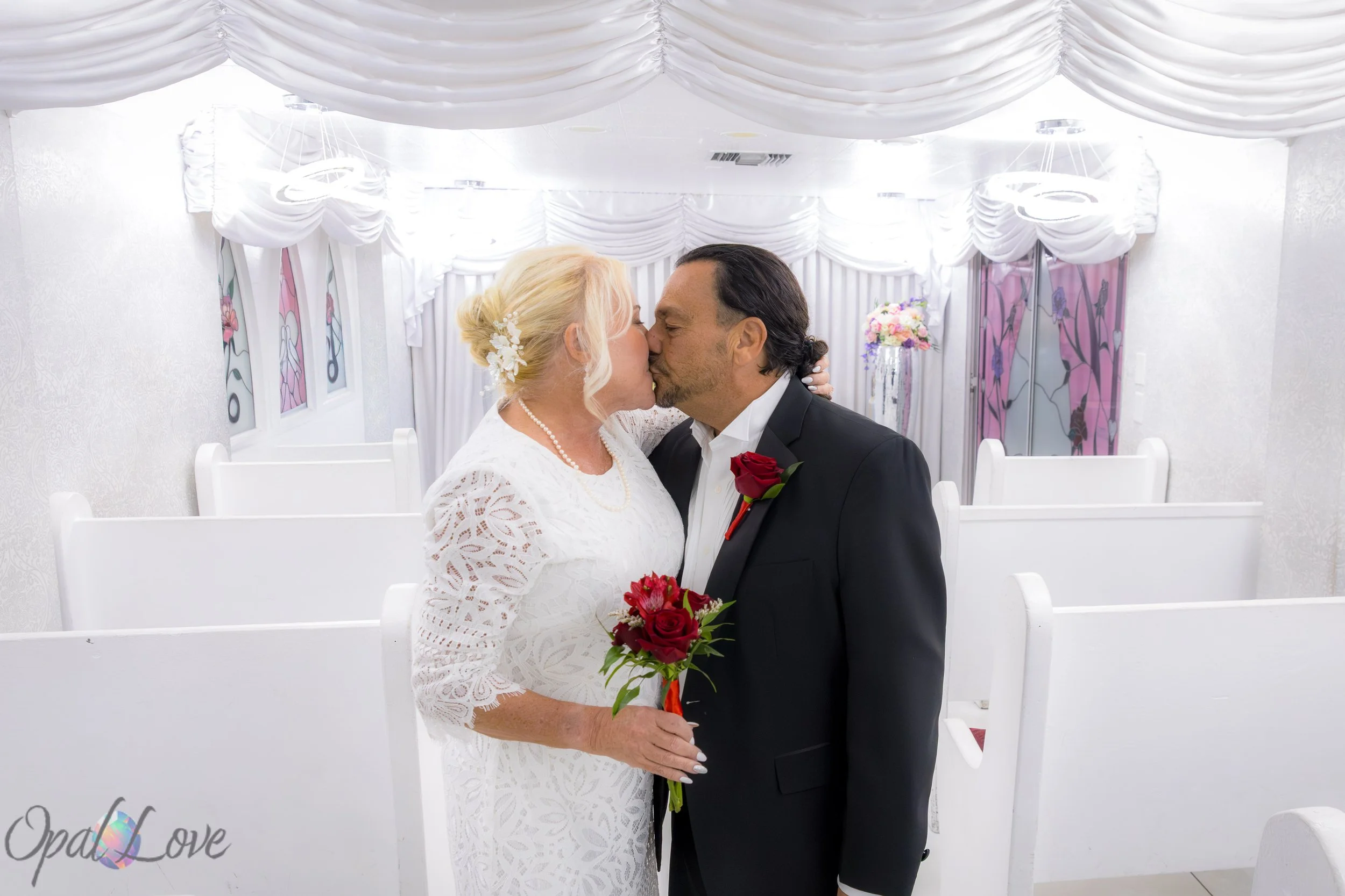 Bride and groom sharing a kiss in the chapel aisle under white draping at A Little White Wedding Chapel.