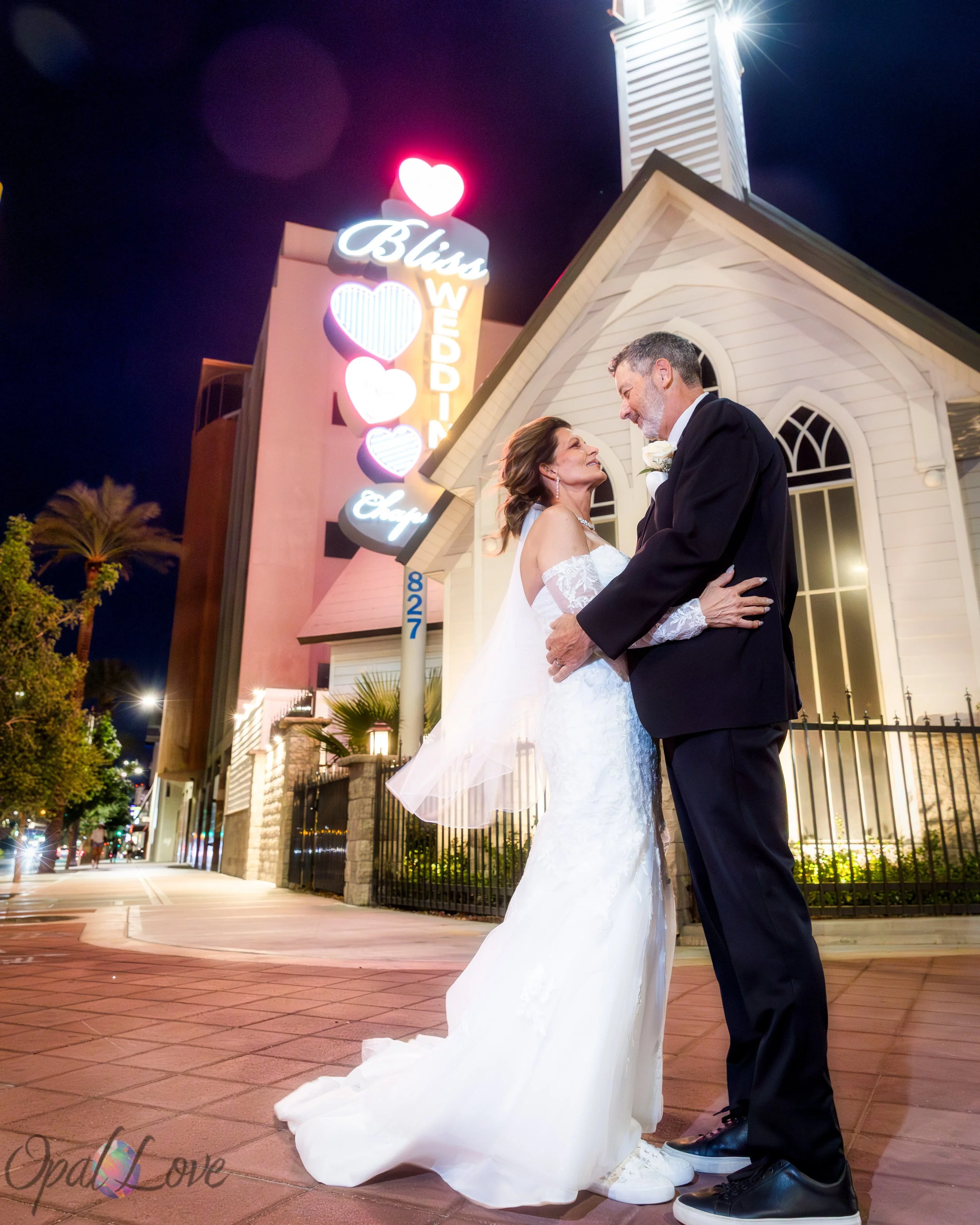 Bride and groom embracing outside the illuminated Bliss Wedding Chapel at night.
