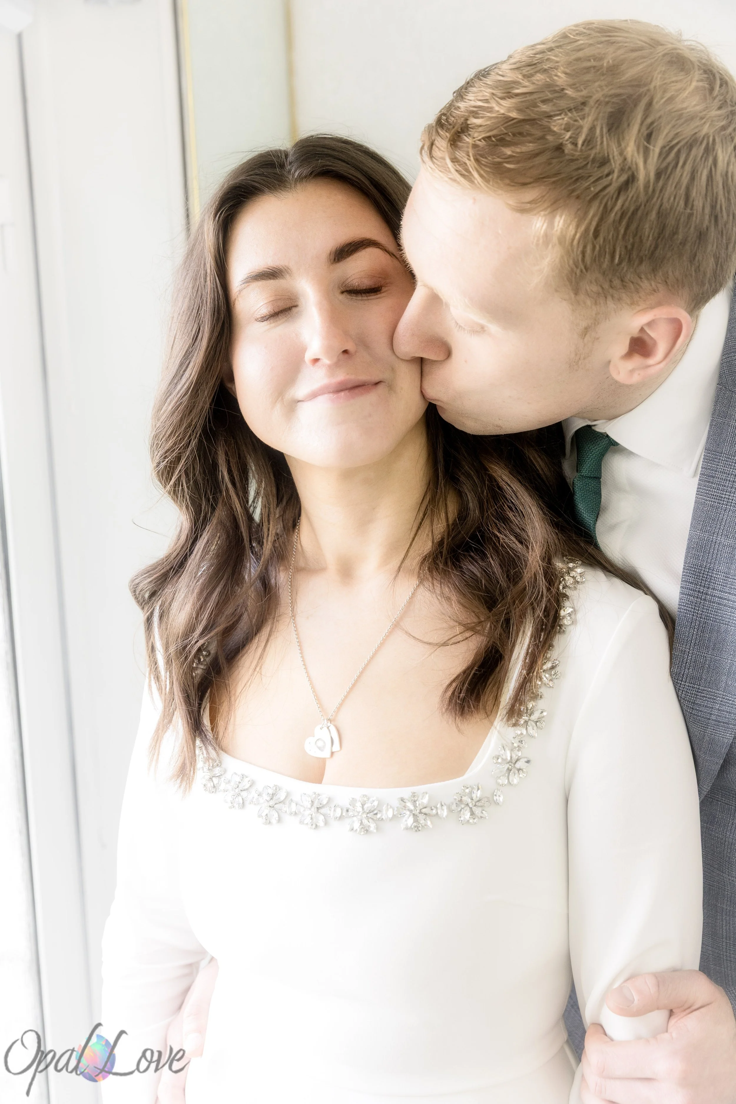 Groom kissing bride on the cheek by a bright window inside the chapel during their Las Vegas wedding.