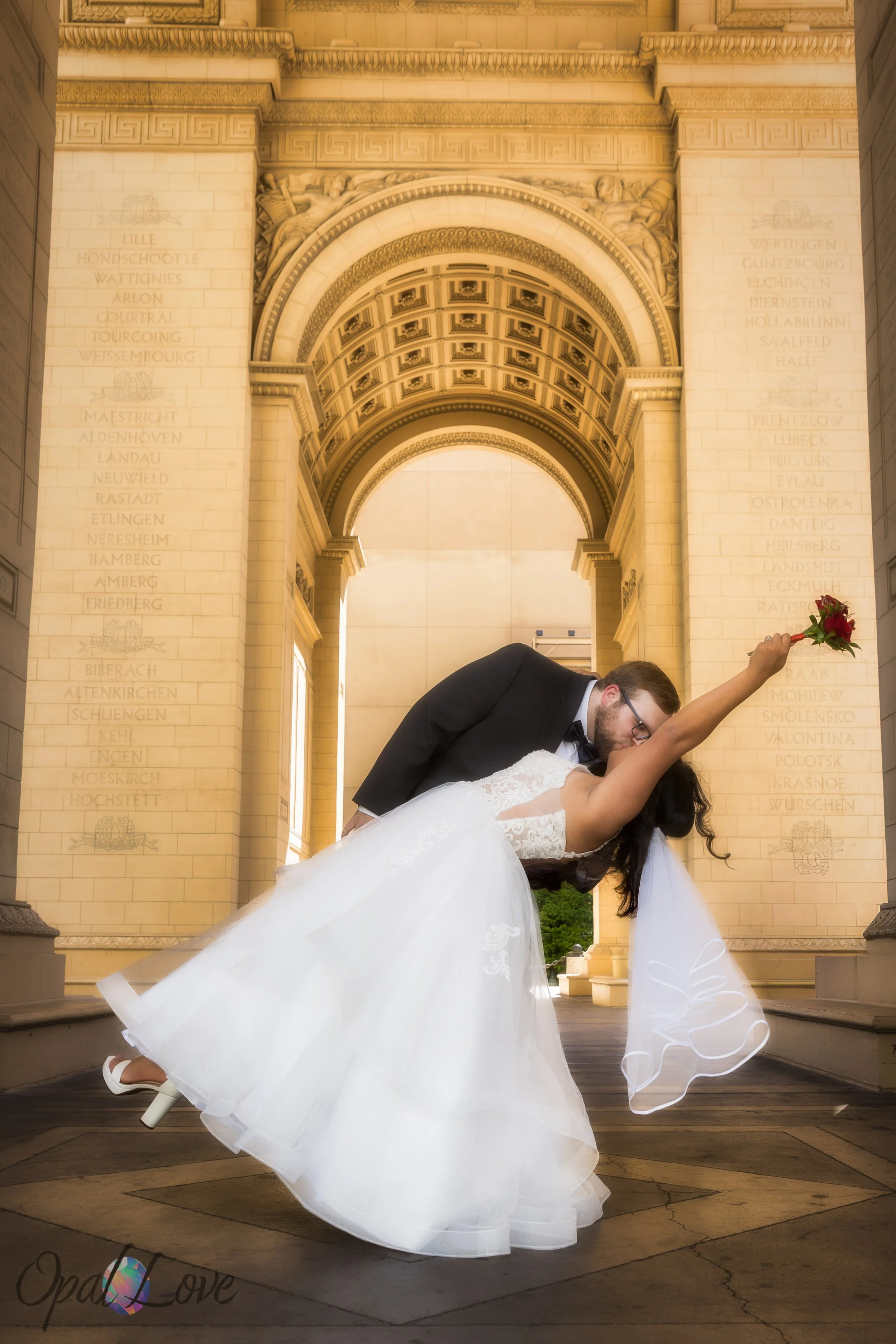 Groom dipping bride for a kiss beneath ornate arch at Paris Las Vegas.
