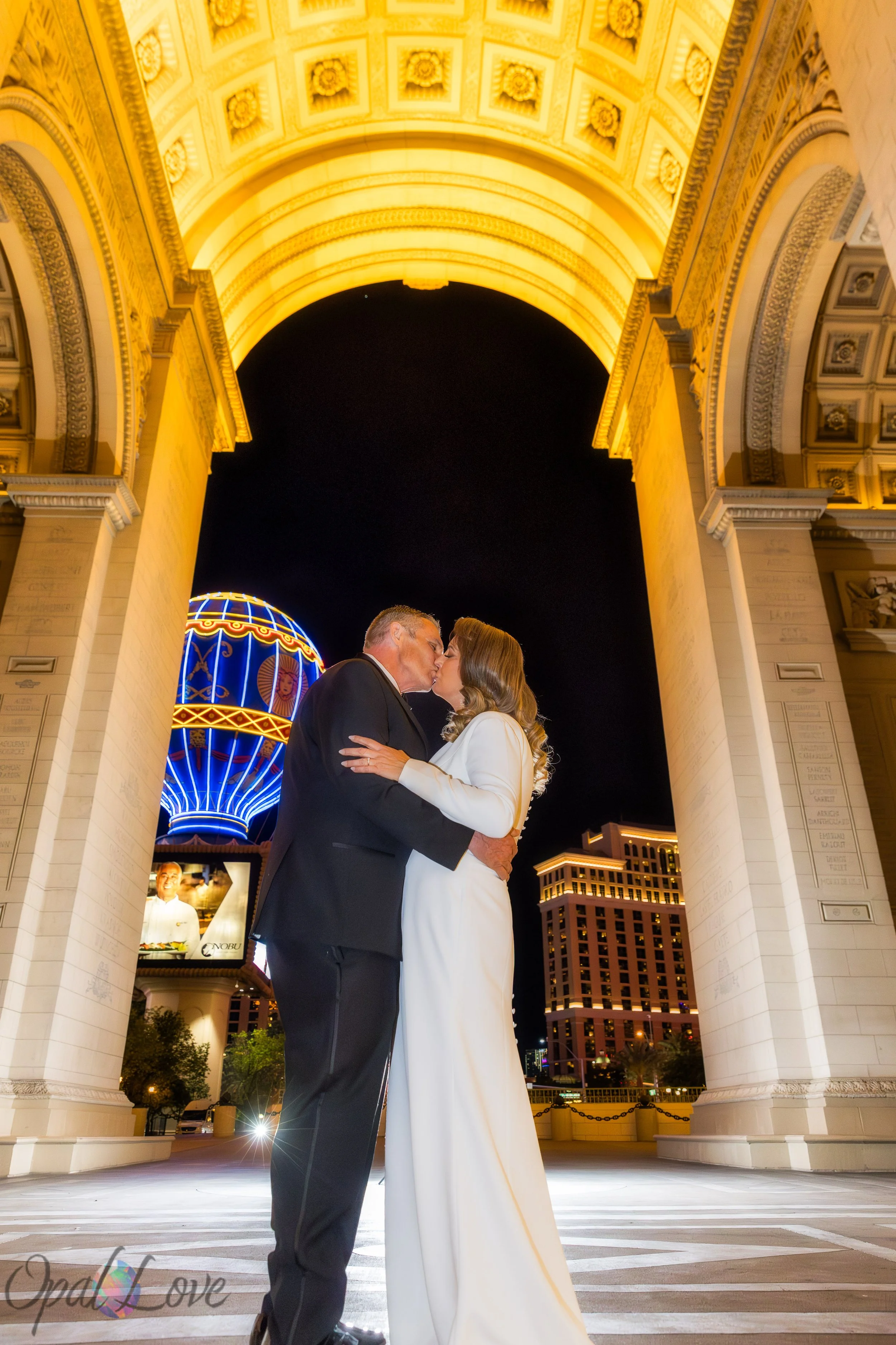 Couple kissing under Paris Las Vegas archway with illuminated Strip background