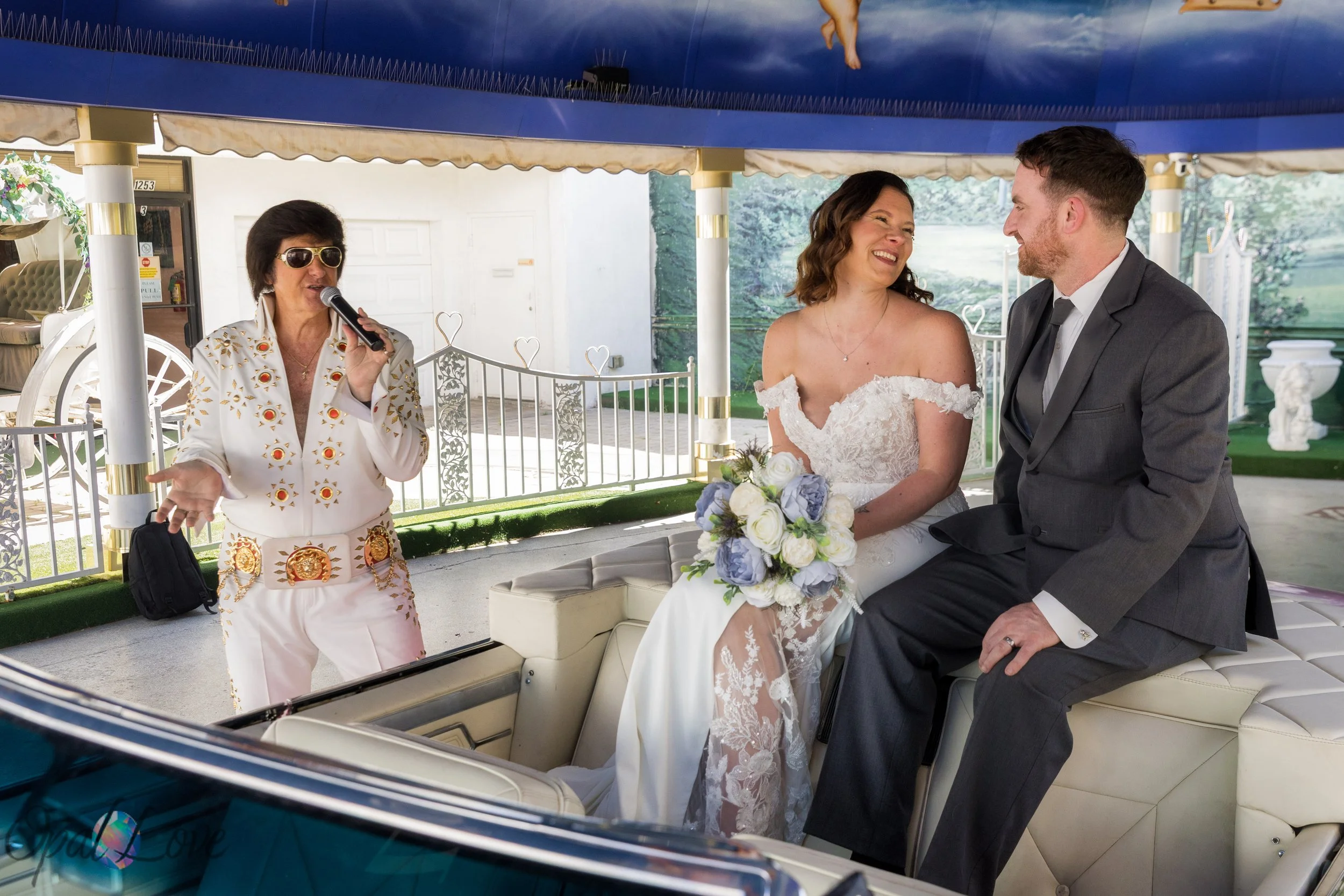 Elvis officiating a Las Vegas drive up wedding ceremony for a couple seated in a pink Cadillac at Little White Chapel.