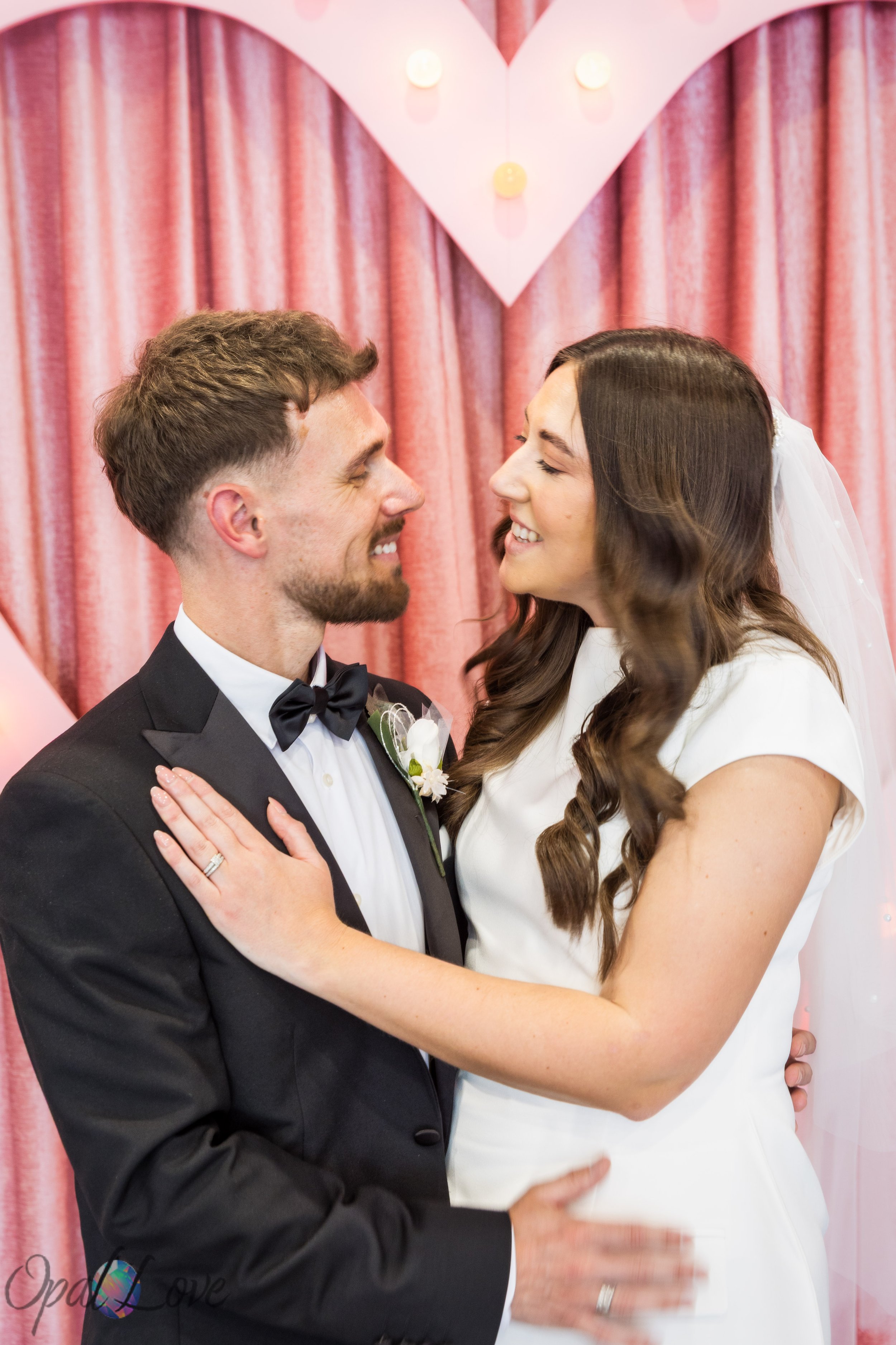 Newly married couple smiling together in front of pink heart backdrop at Las Vegas vow renewal ceremony