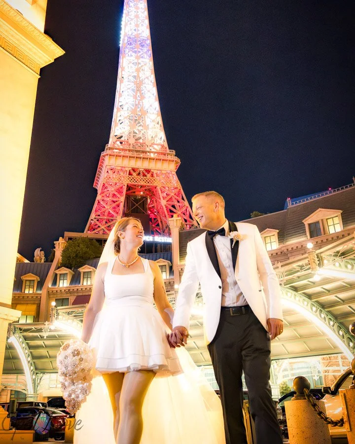 Couple walking hand in hand beneath the Eiffel Tower at Paris Las Vegas at night.