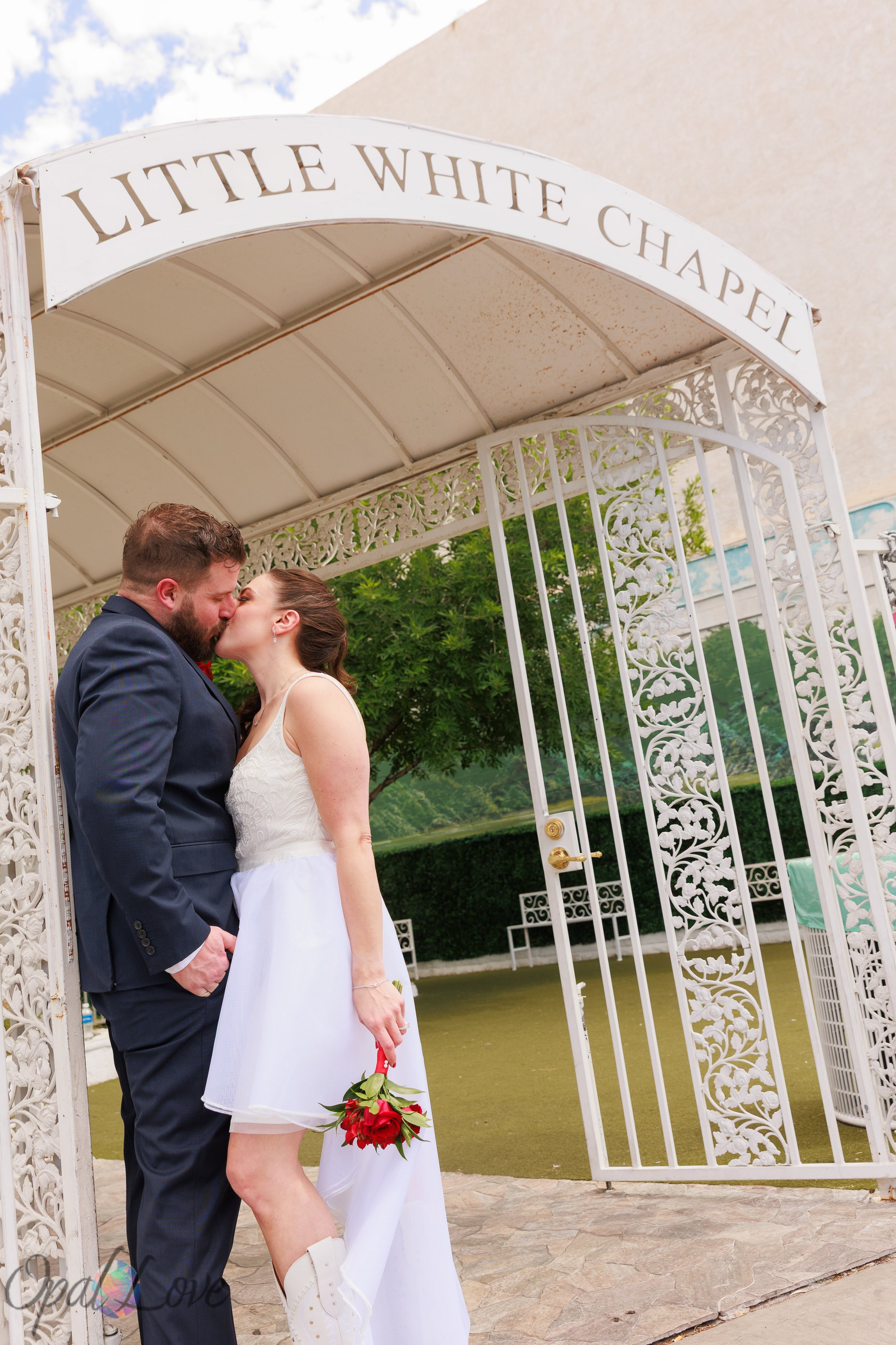 Couple kissing beneath the white garden arch at the Little White Chapel.
