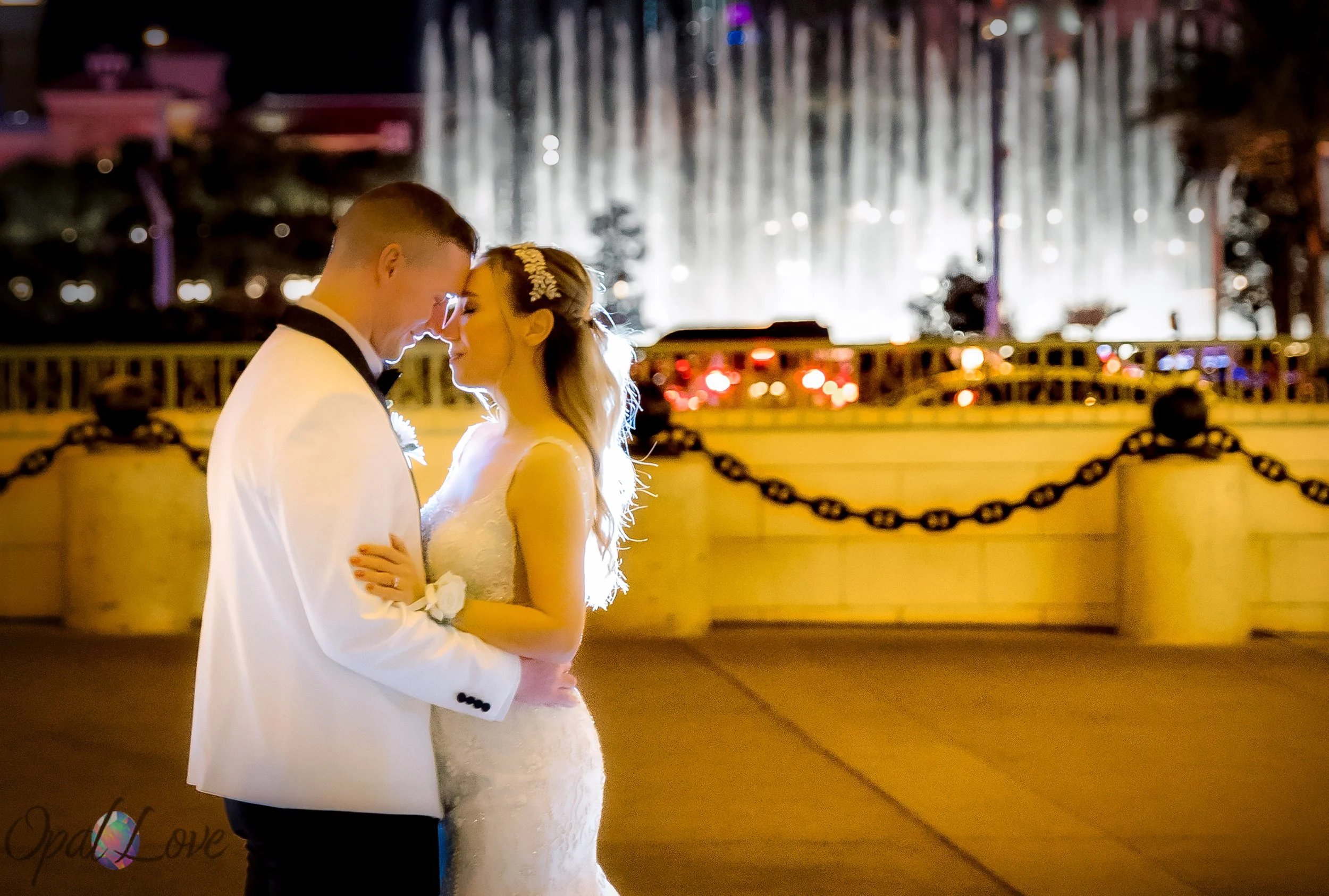 Newlyweds touching foreheads with the Bellagio fountains glowing behind them at night.