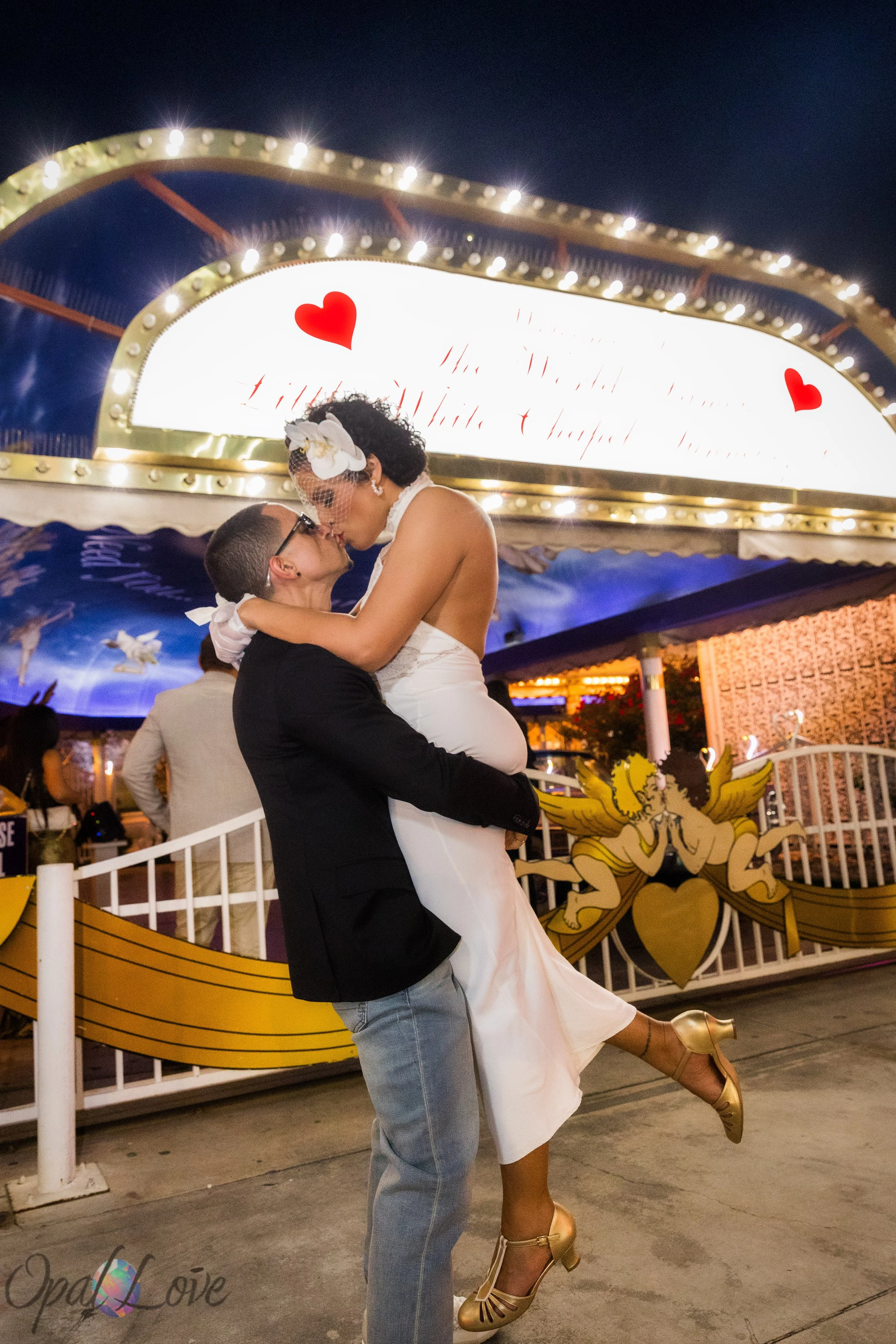 Groom lifting bride for a kiss outside the Little White Wedding Chapel at night in Las Vegas.