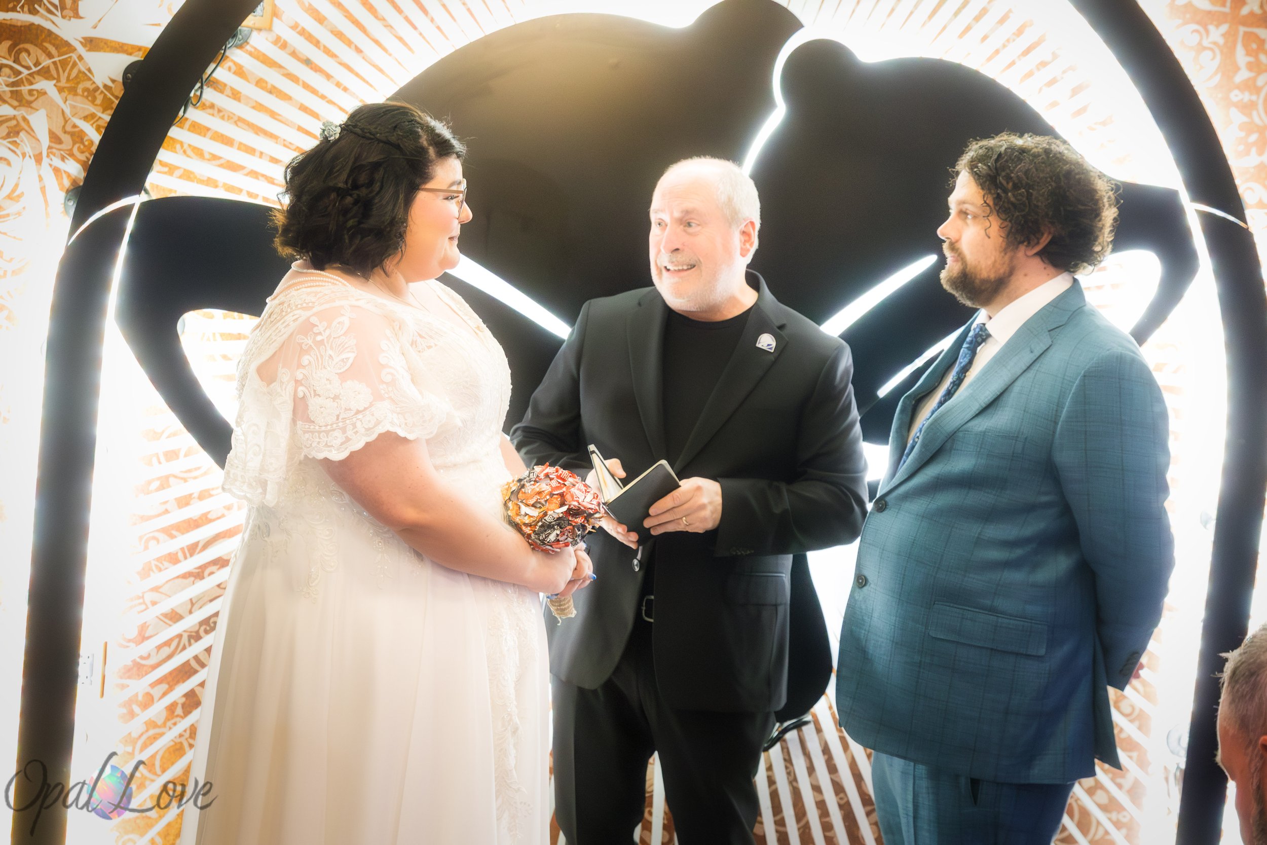 Couple standing with their officiant under the glowing Taco Bell Cantina wedding arch.