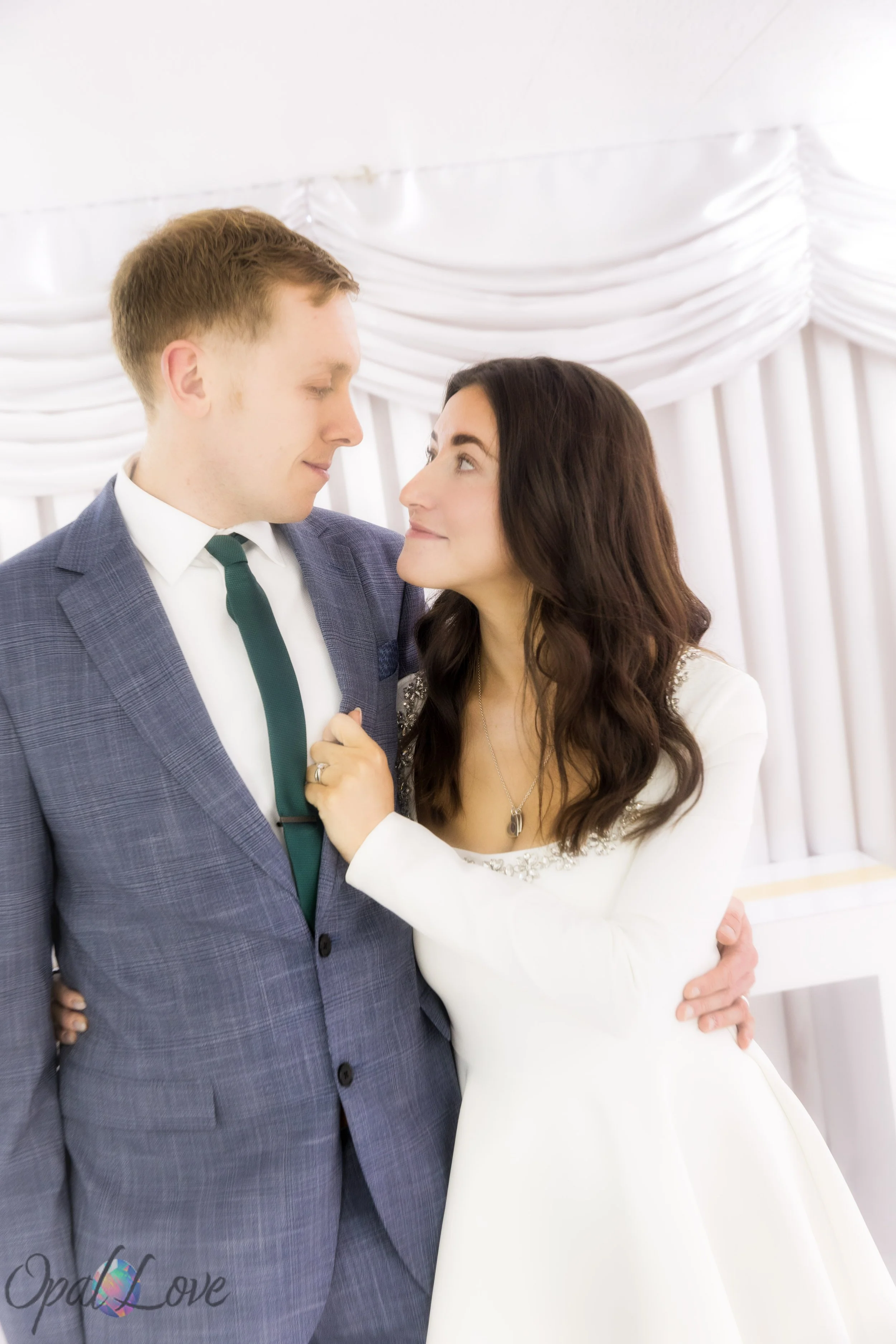 Bride and groom embracing in front of white drapery inside A Little White Wedding Chapel after their ceremony.