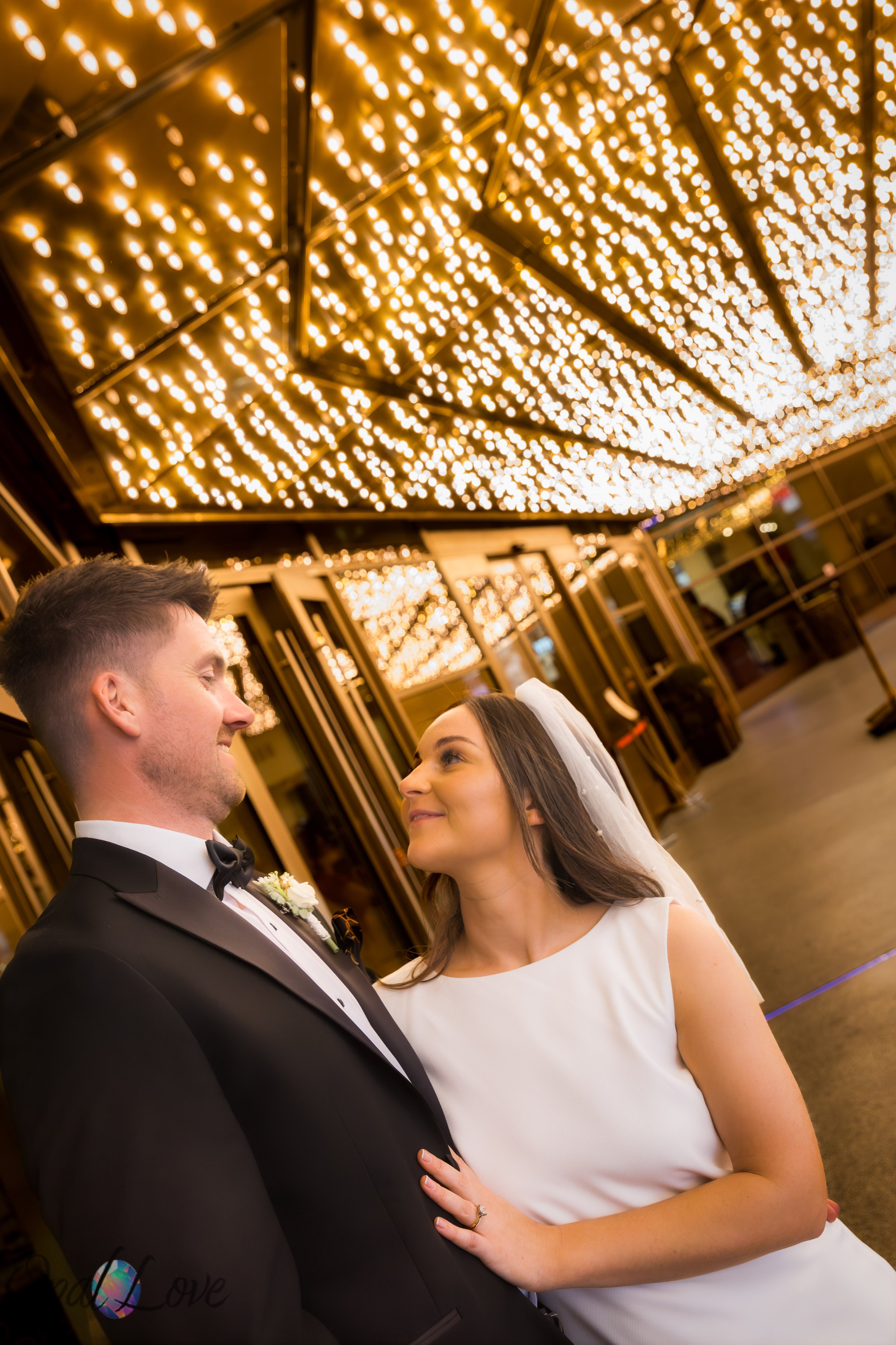 Newlyweds share a quiet moment beneath the warm carousel-style lights of the Plaza in downtown Las Vegas.