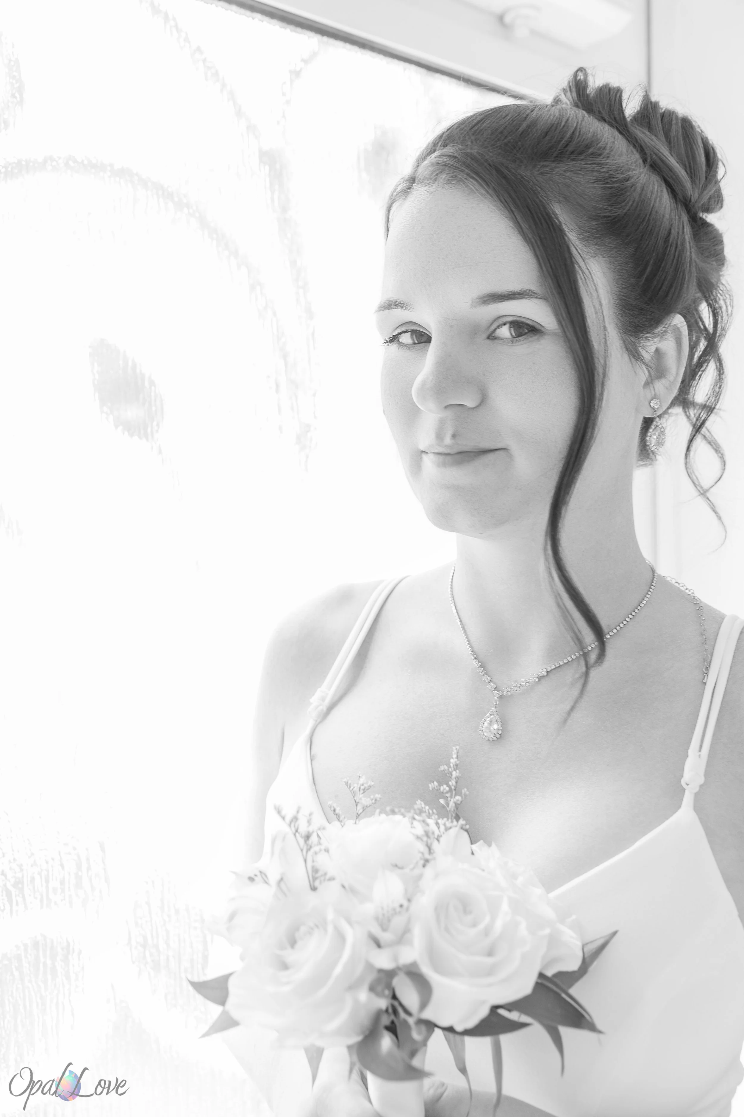 Bride holding bouquet by window in black and white portrait