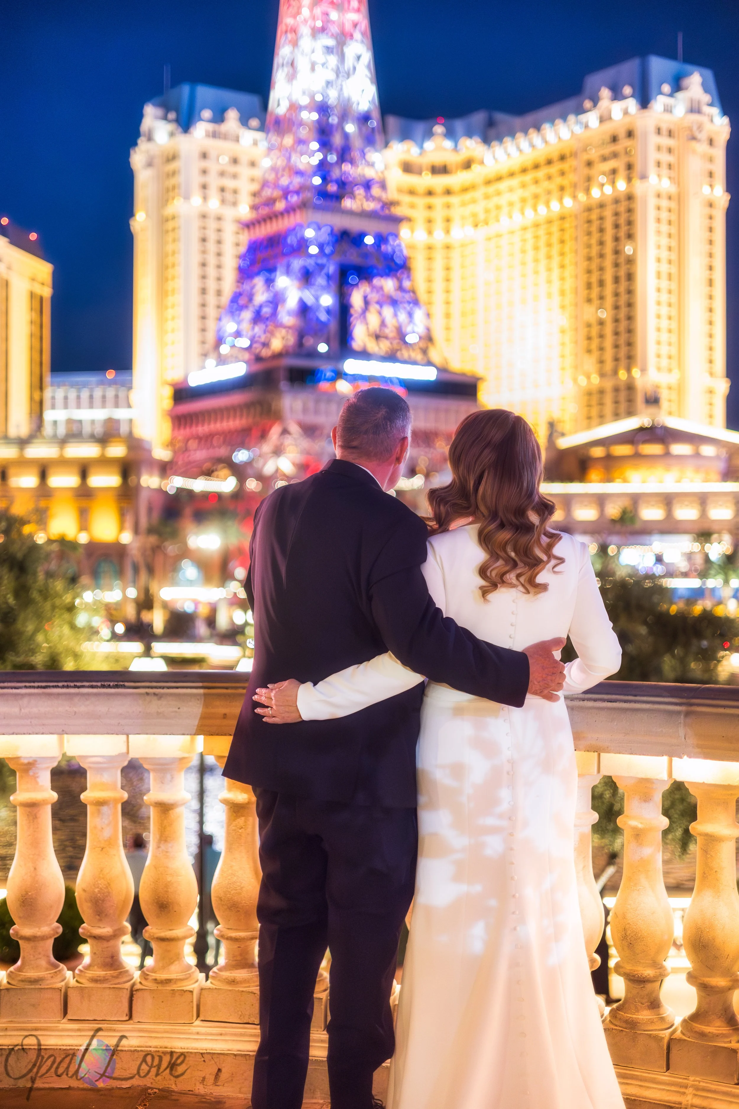 Couple standing together at Bellagio with Paris Las Vegas Eiffel Tower glowing in the background at night