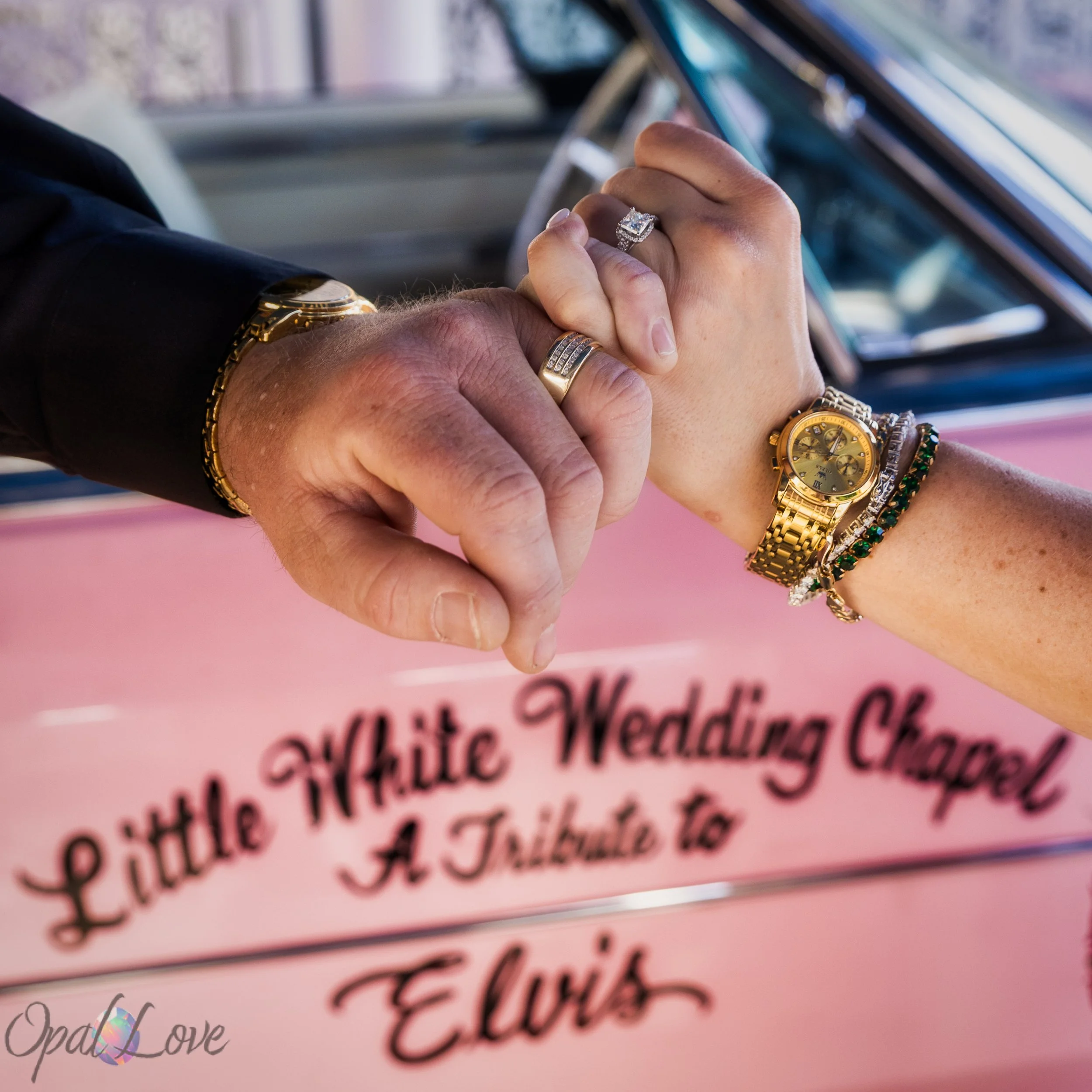 Close up of wedding rings in front of Little White Wedding Chapel pink Cadillac