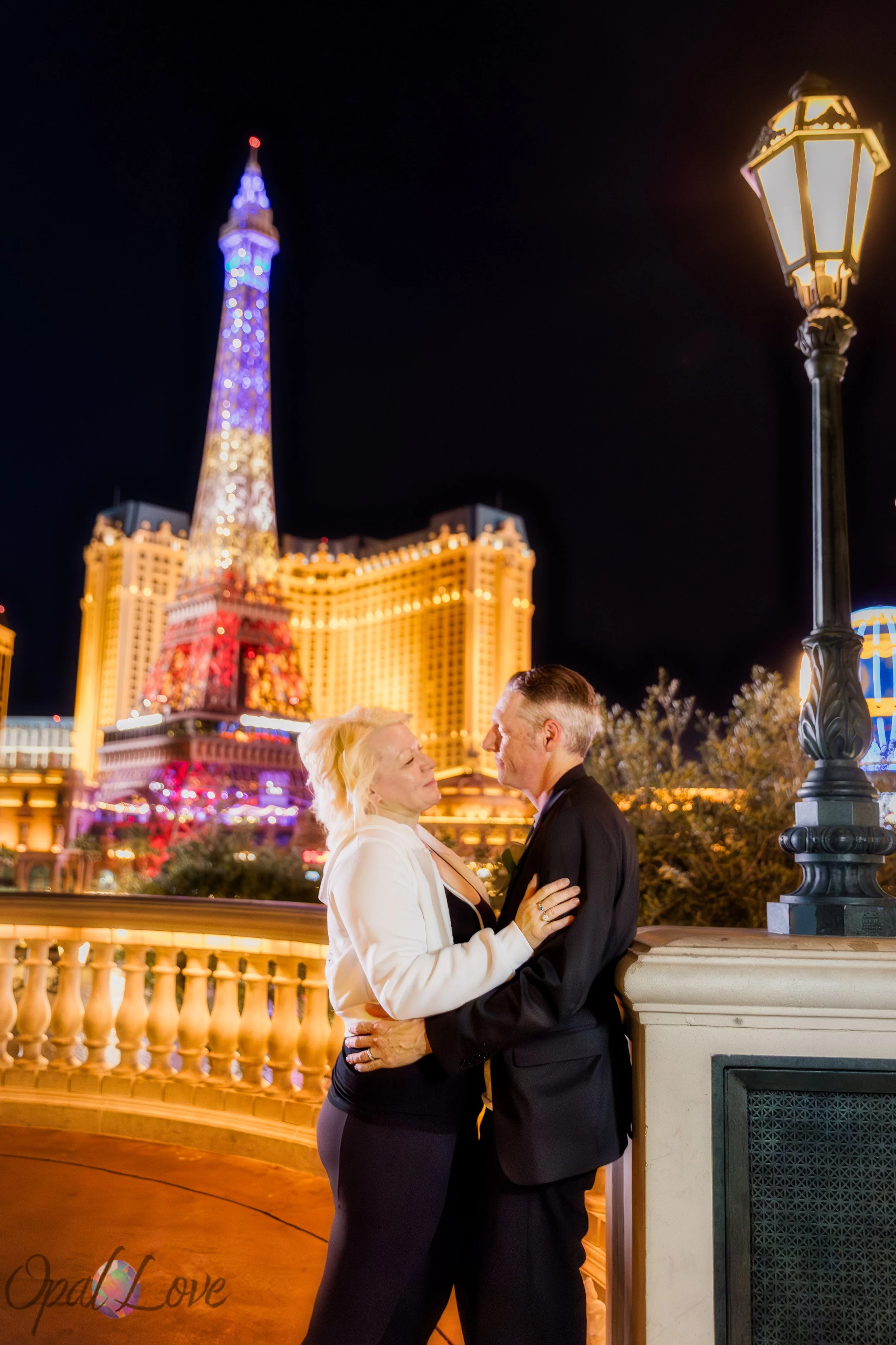 Couple standing together at night on the Strip with Paris Las Vegas Eiffel Tower illuminated behind them