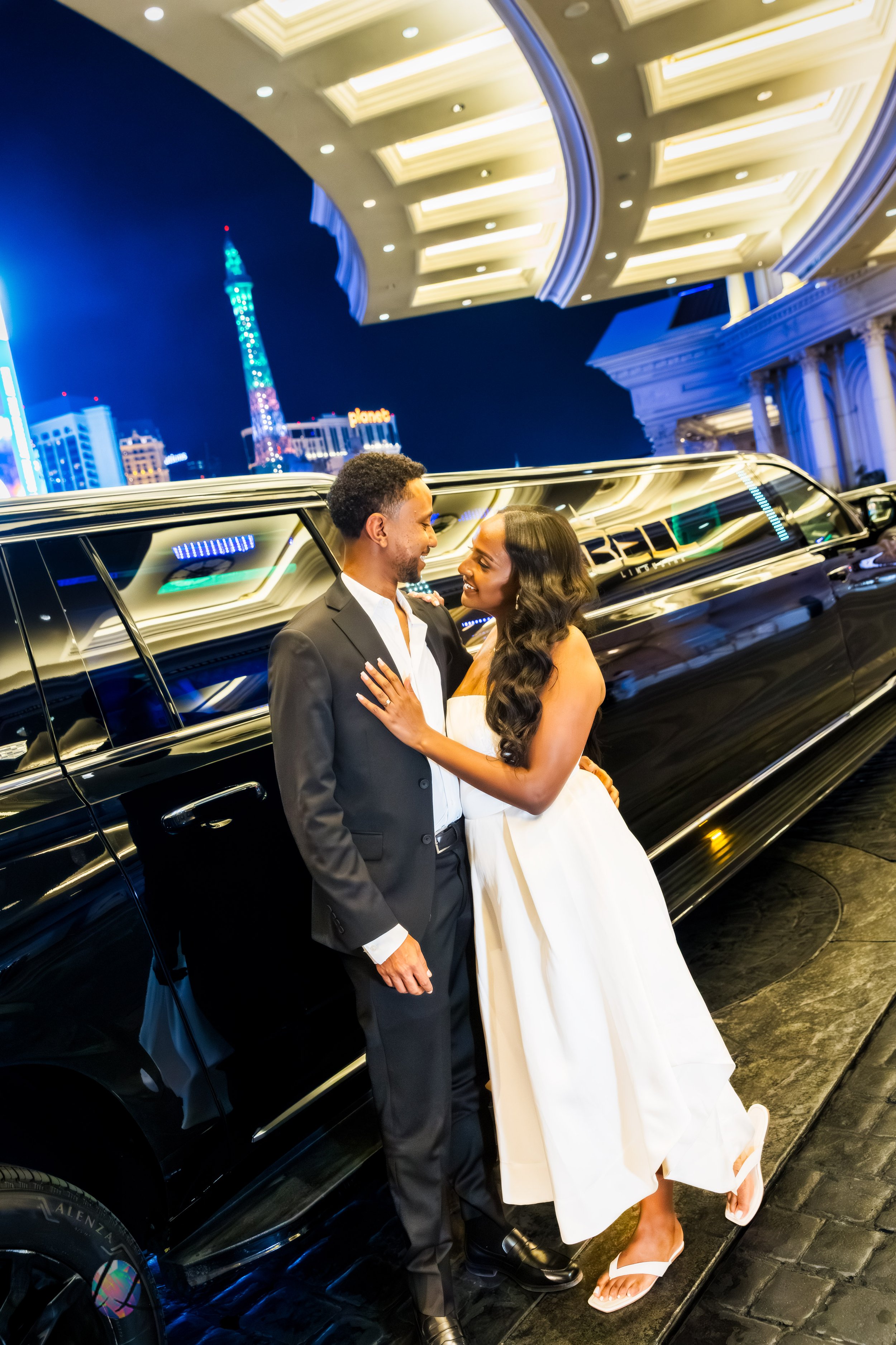 Menna and Yoseph posing beside their limousine near Caesars Palace during a nighttime Las Vegas Strip photo tour.
