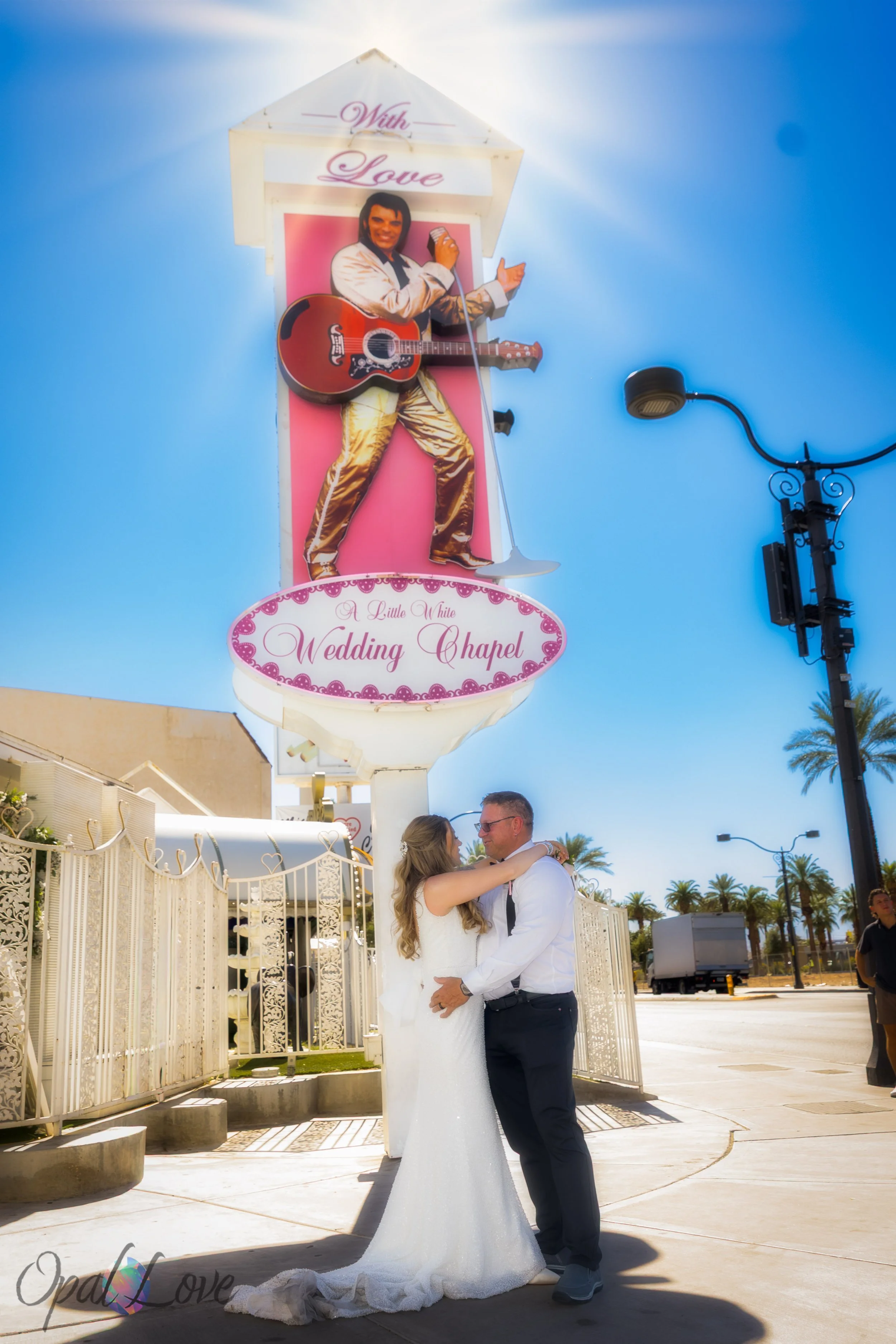 Newlyweds embracing beneath Elvis sign outside Little White Wedding Chapel.