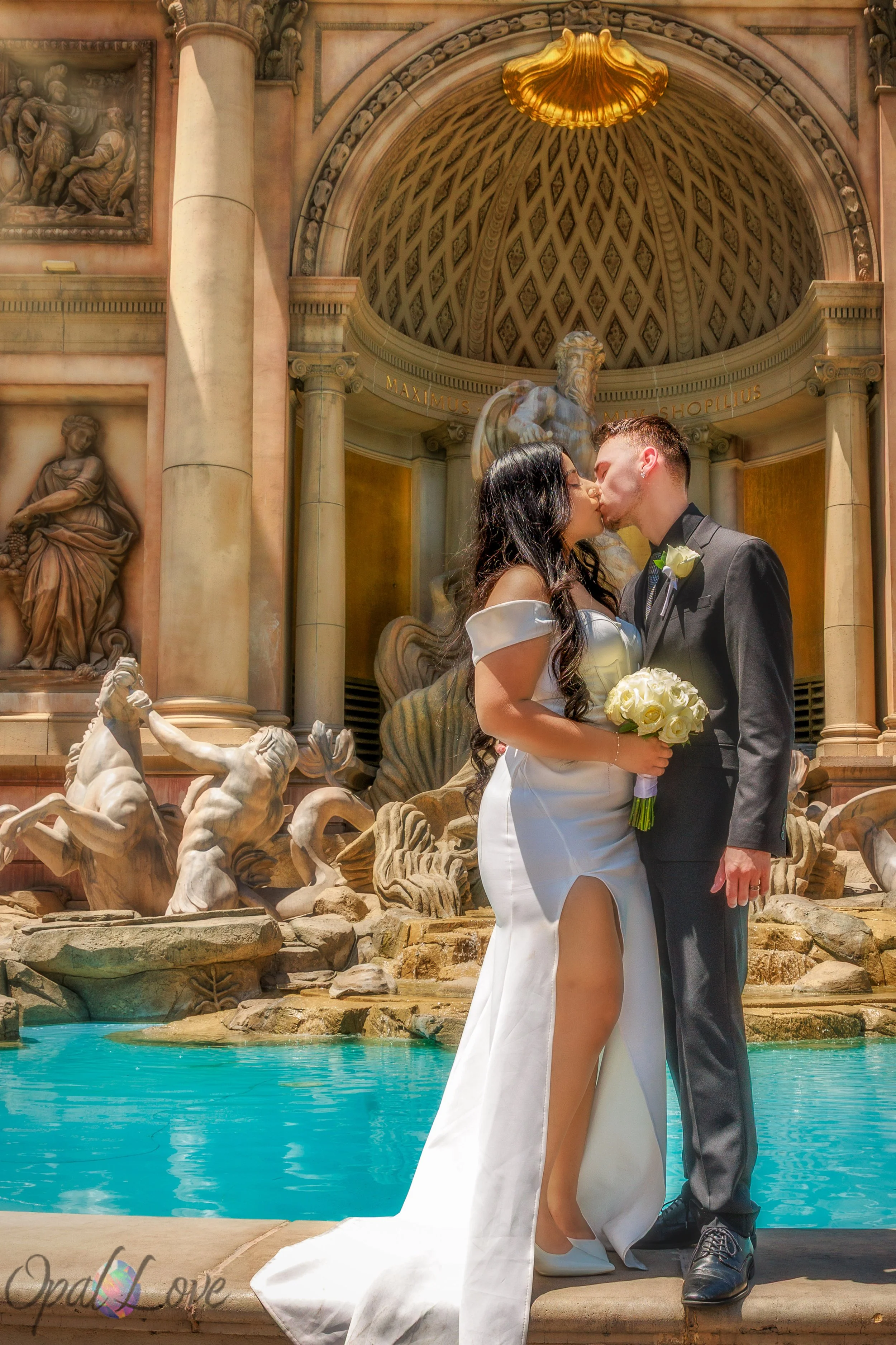 Newlyweds kiss beside the classical sculptures and turquoise water of the Trevi Fountain in Las Vegas.