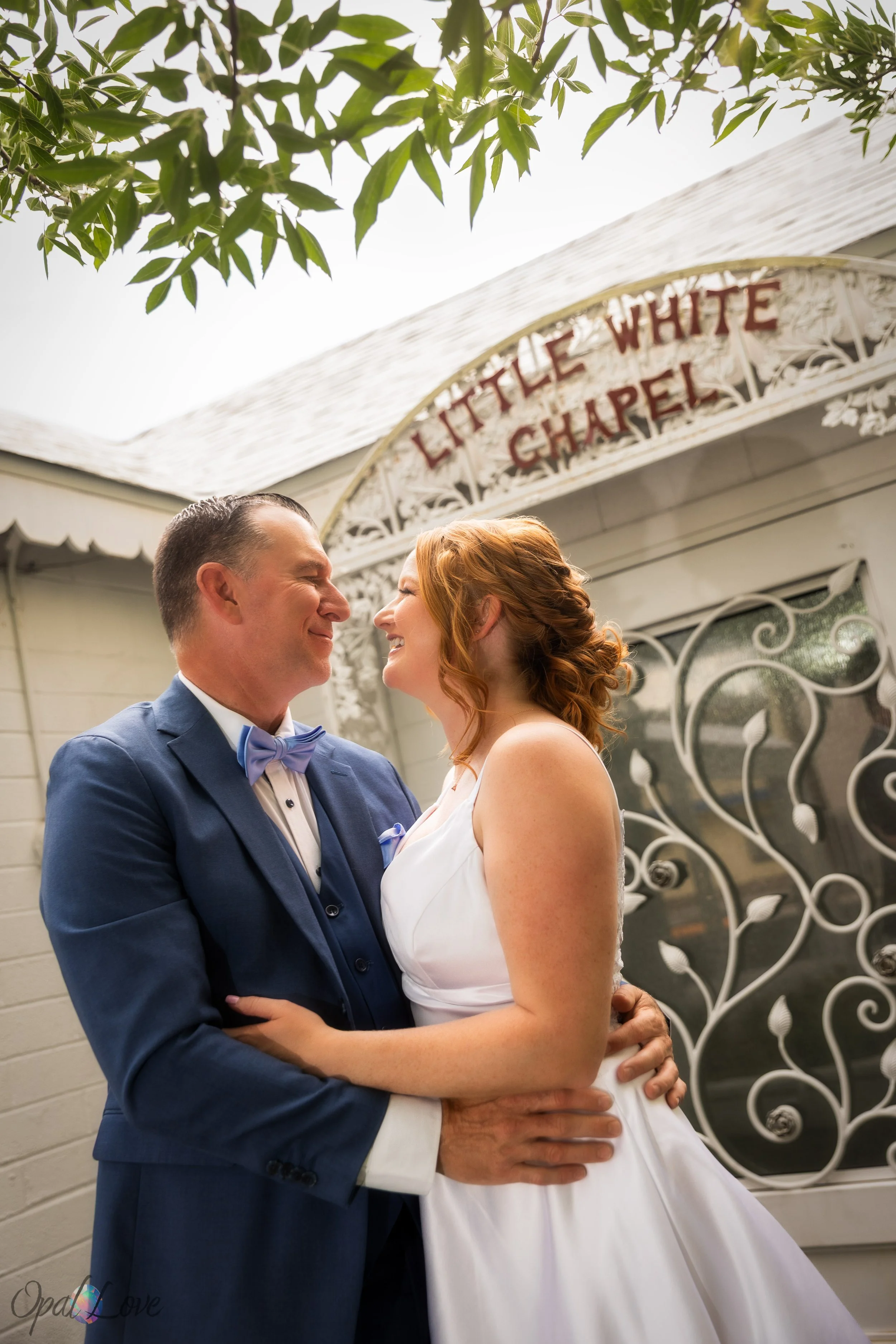 Couple smiling at each other in front of the Little White Chapel doors