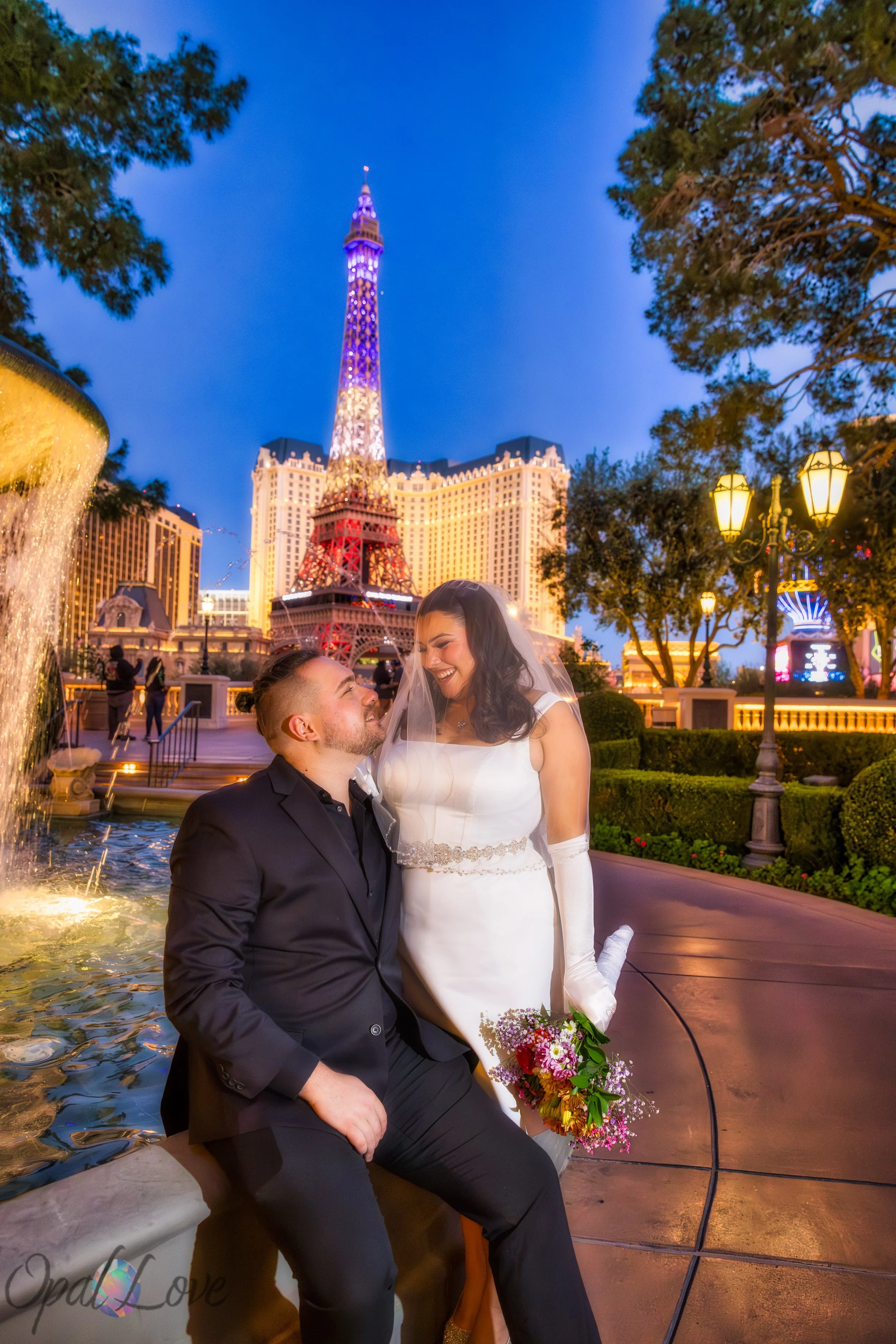 Anniversary couple sitting near the Bellagio fountains with colorful lights reflecting on the water.