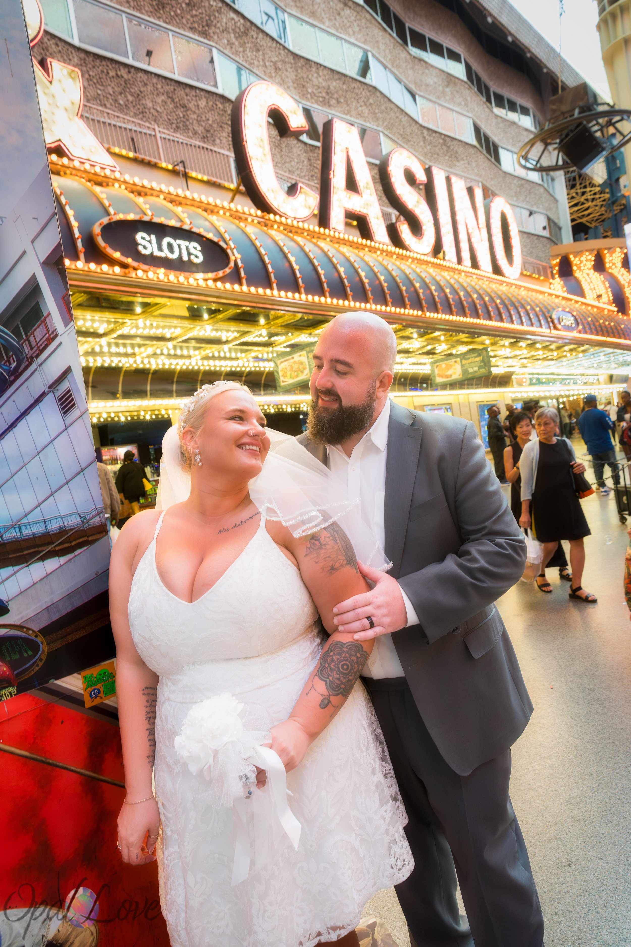 Newlyweds smiling in front of a classic Fremont Street casino entrance with glowing bulbs.