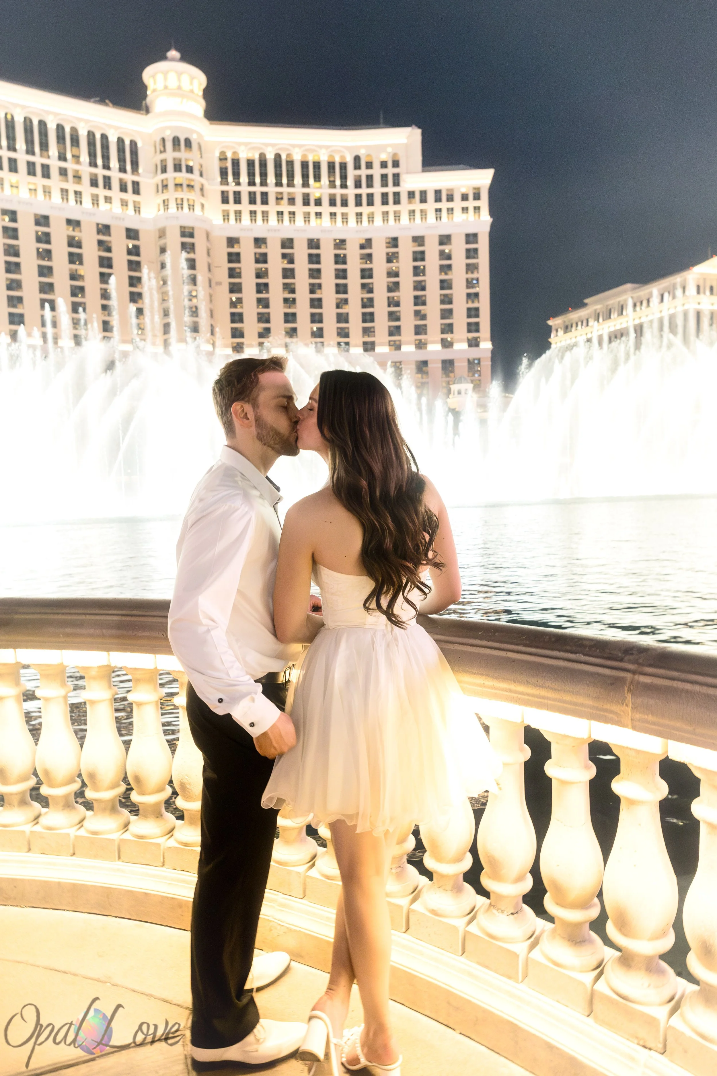 Bride and groom kissing in front of the bright Bellagio fountains during their Las Vegas wedding photo session.