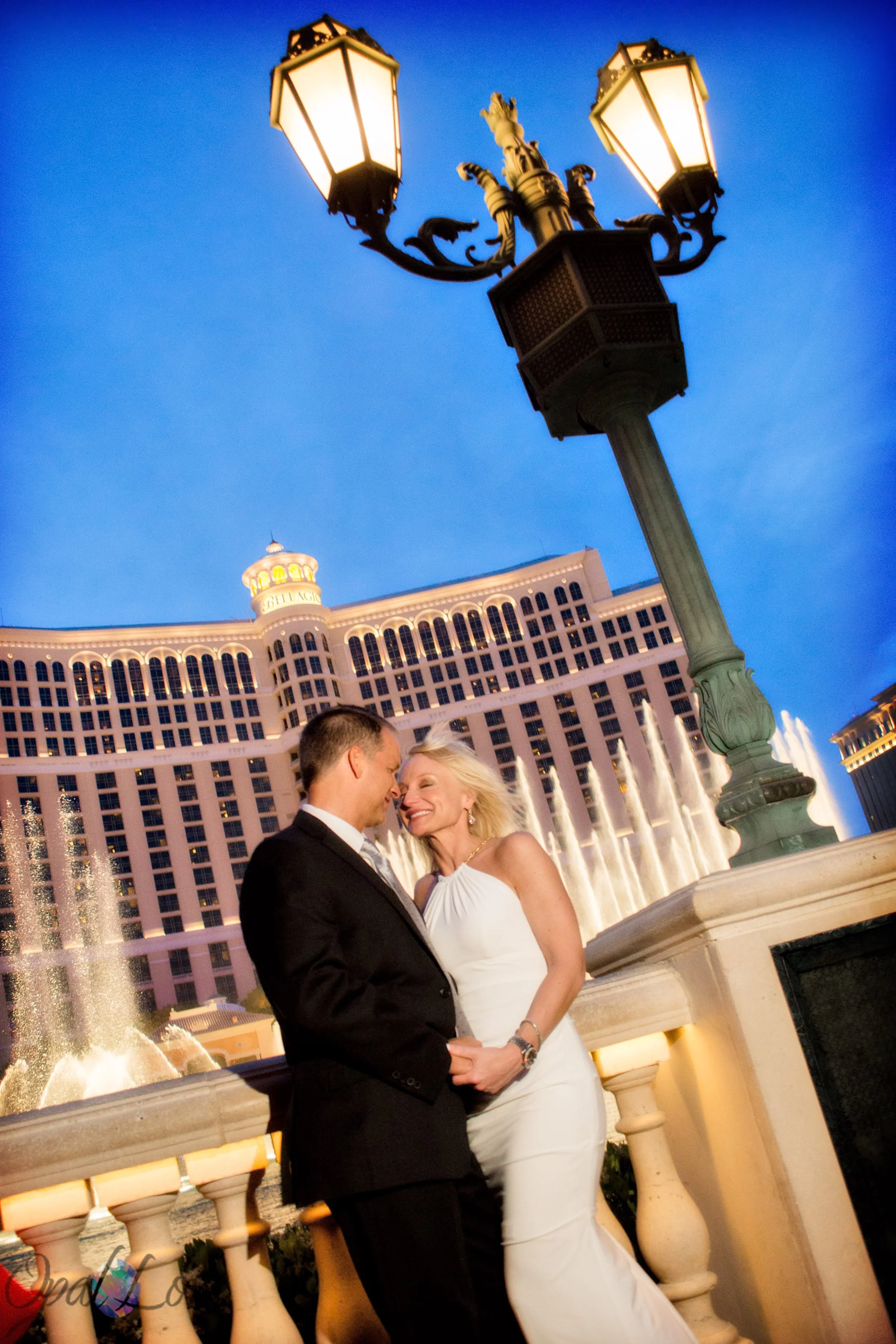 Couple embraces in front of the illuminated Bellagio fountains at twilight in Las Vegas.