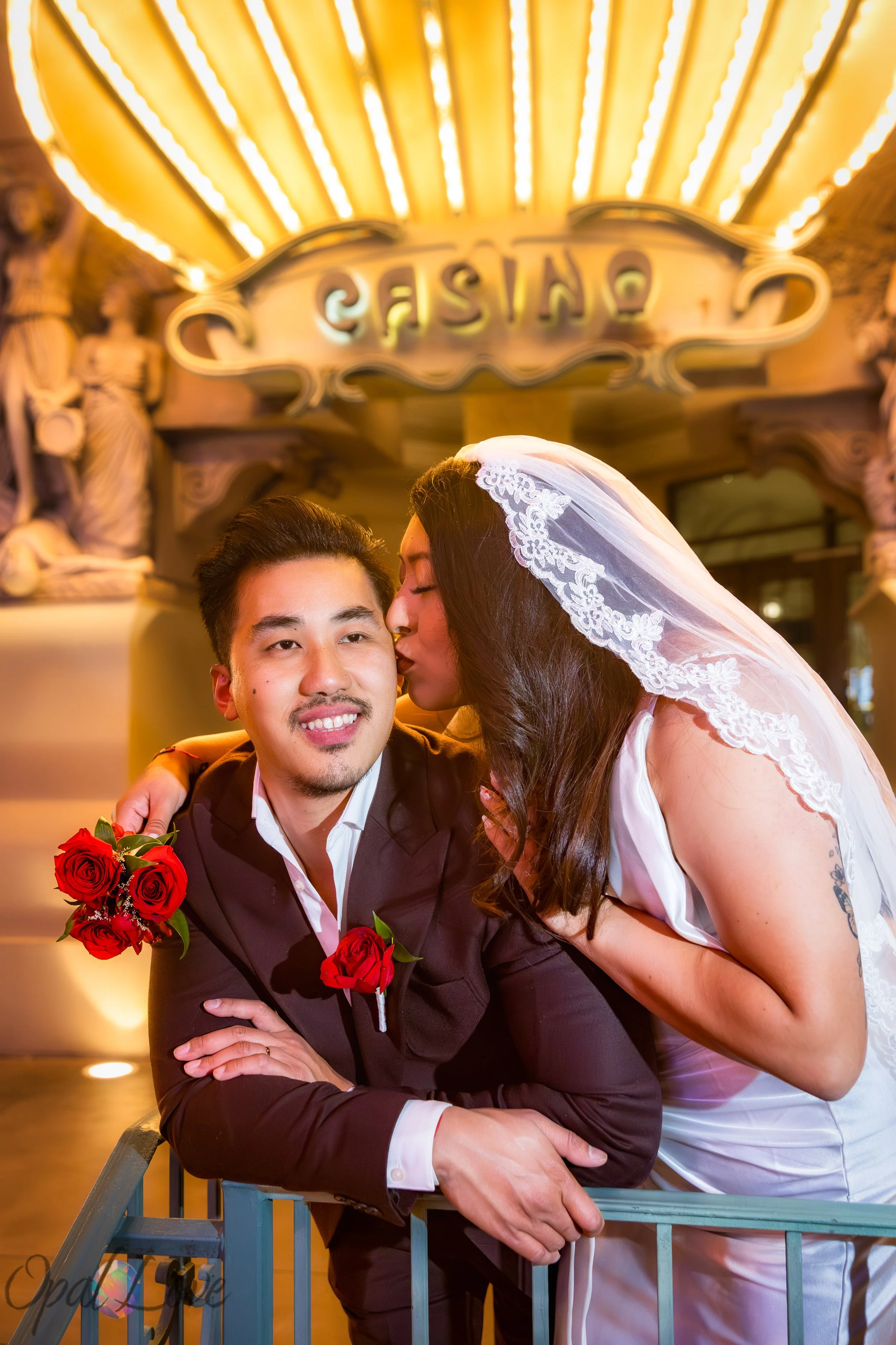 Bride kissing groom beneath the glowing Paris Las Vegas casino entrance lights after their Vegas wedding.