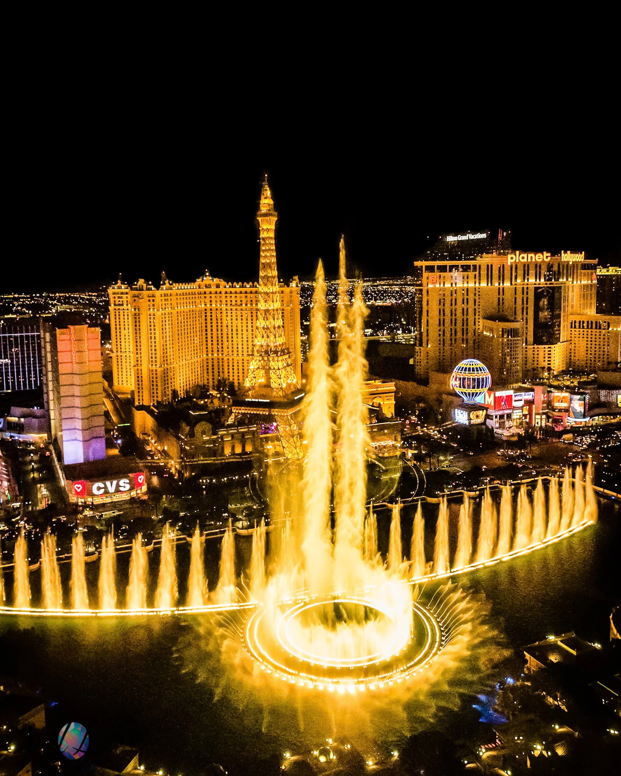 Bellagio fountains and the illuminated Las Vegas Strip viewed from above at night.
