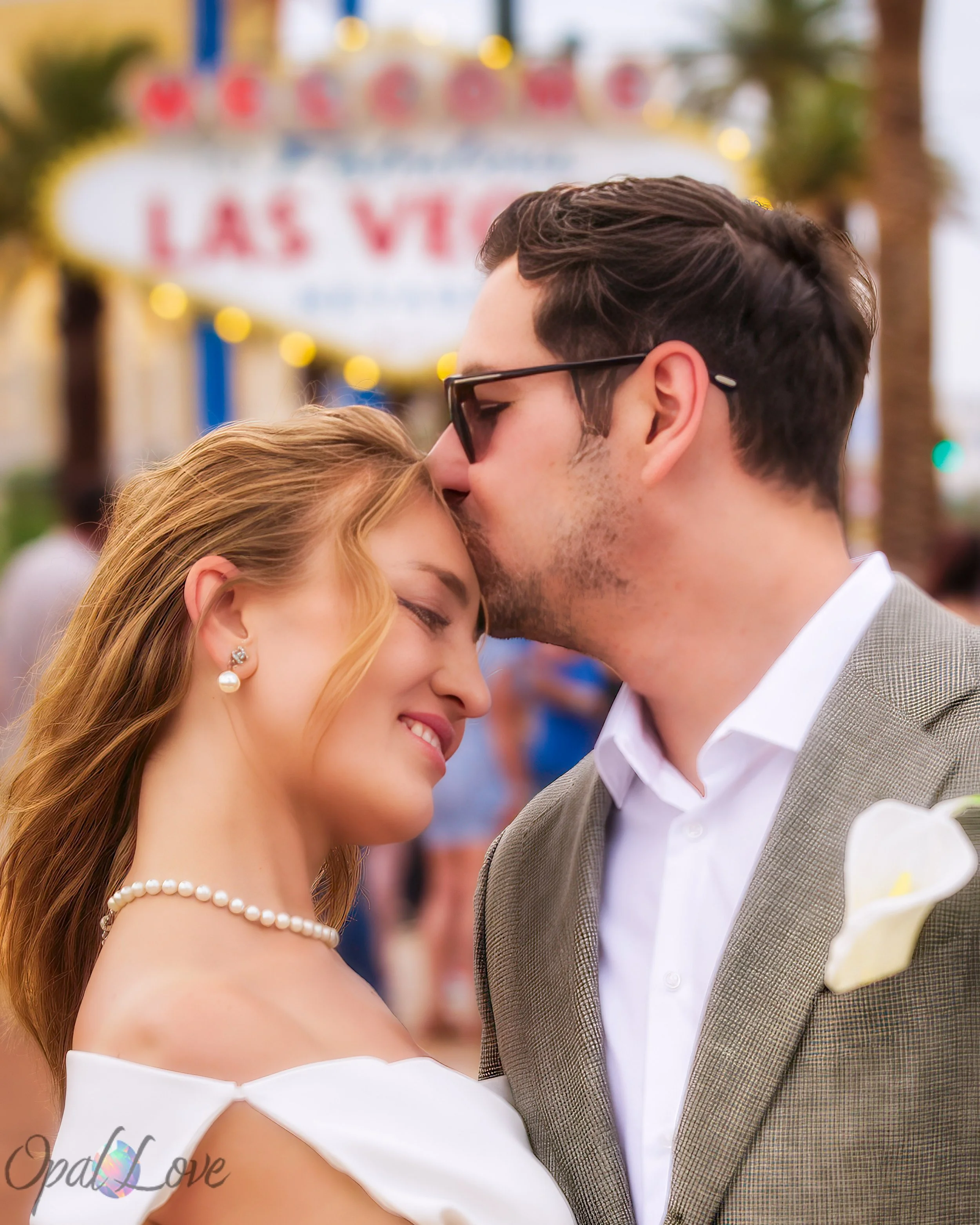 Groom kissing his bride on the forehead in front of the Welcome to Fabulous Las Vegas sign