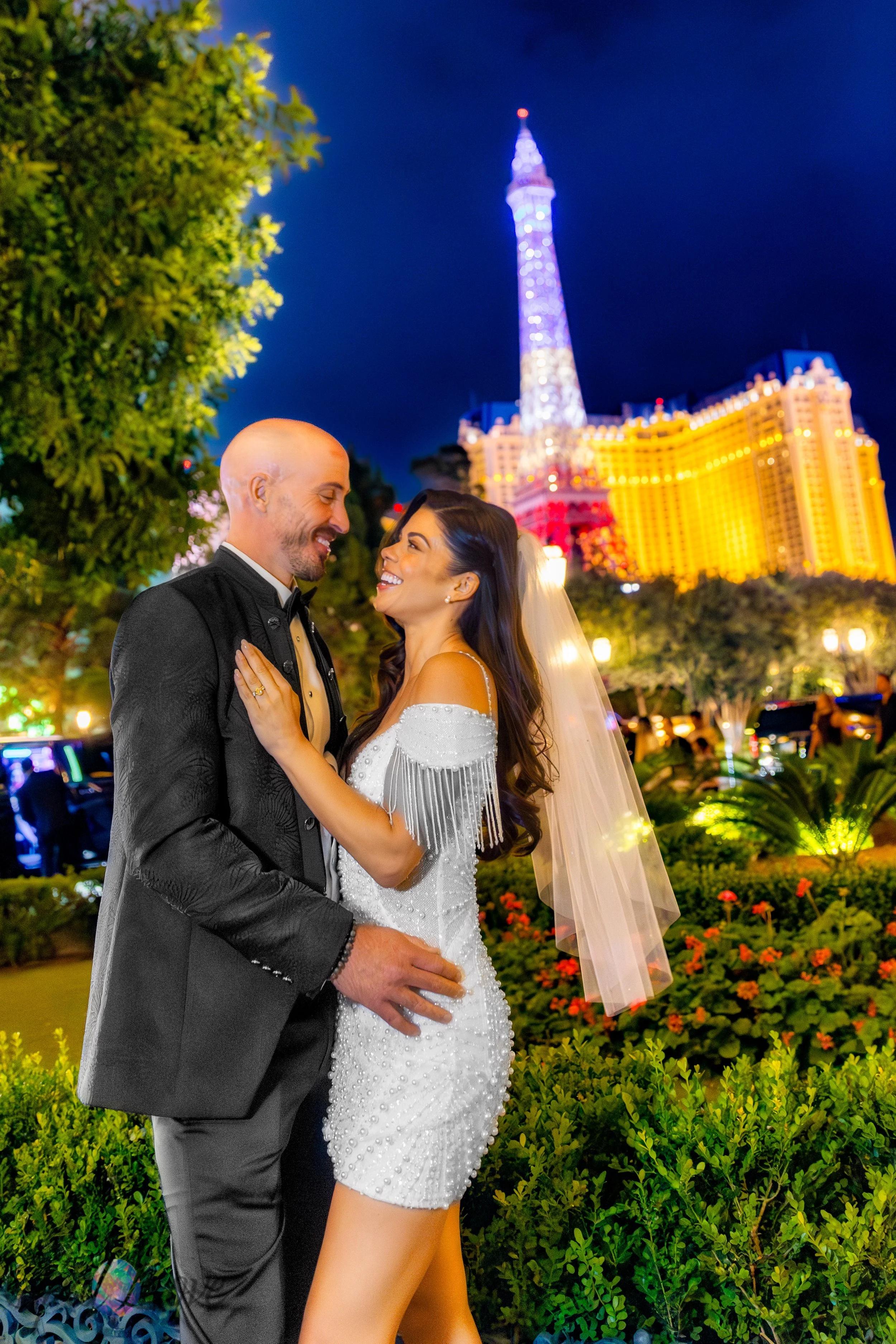 Couple embracing in Bellagio gardens with Paris Las Vegas Eiffel Tower glowing behind