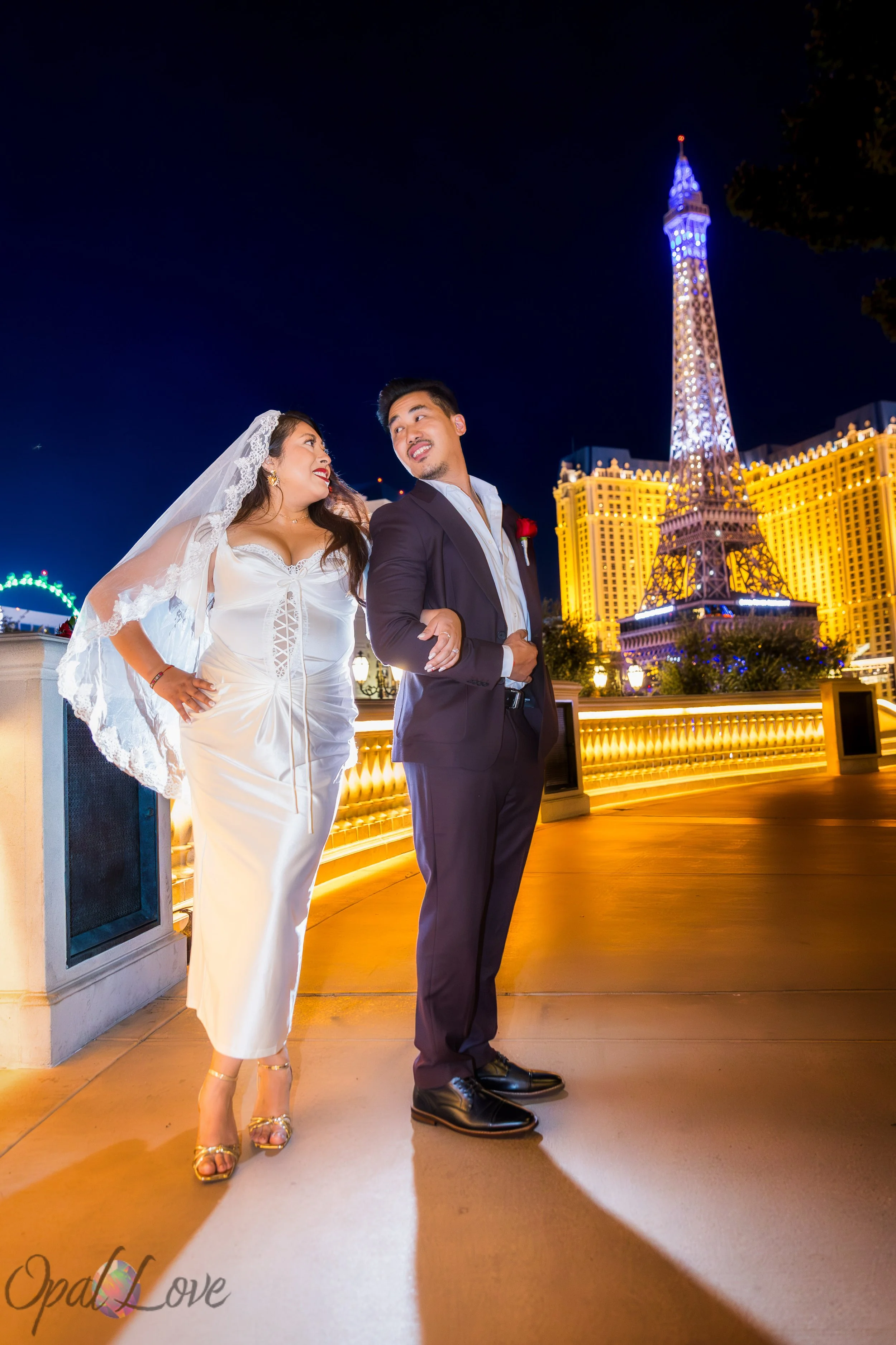 Bride and groom walking together along the Bellagio terrace with the illuminated Eiffel Tower at Paris Las Vegas behind them.