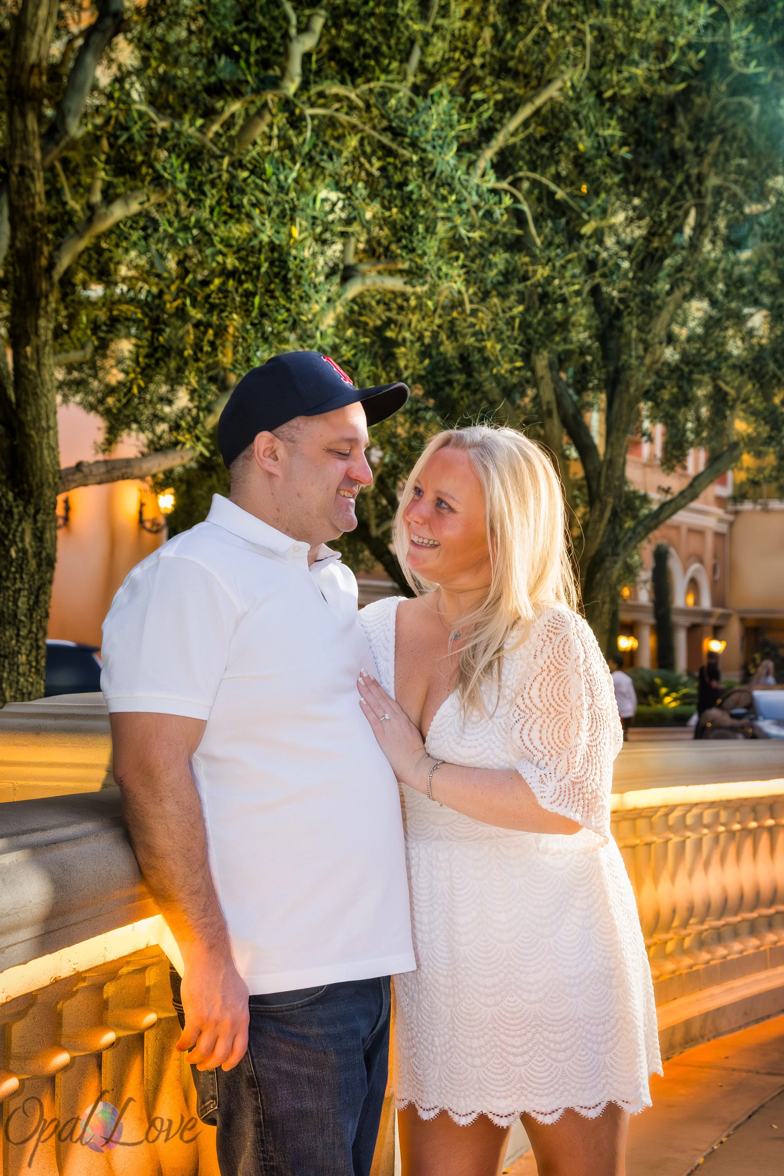 Couple standing close under warm lights near Bellagio trees during their engagement photos.