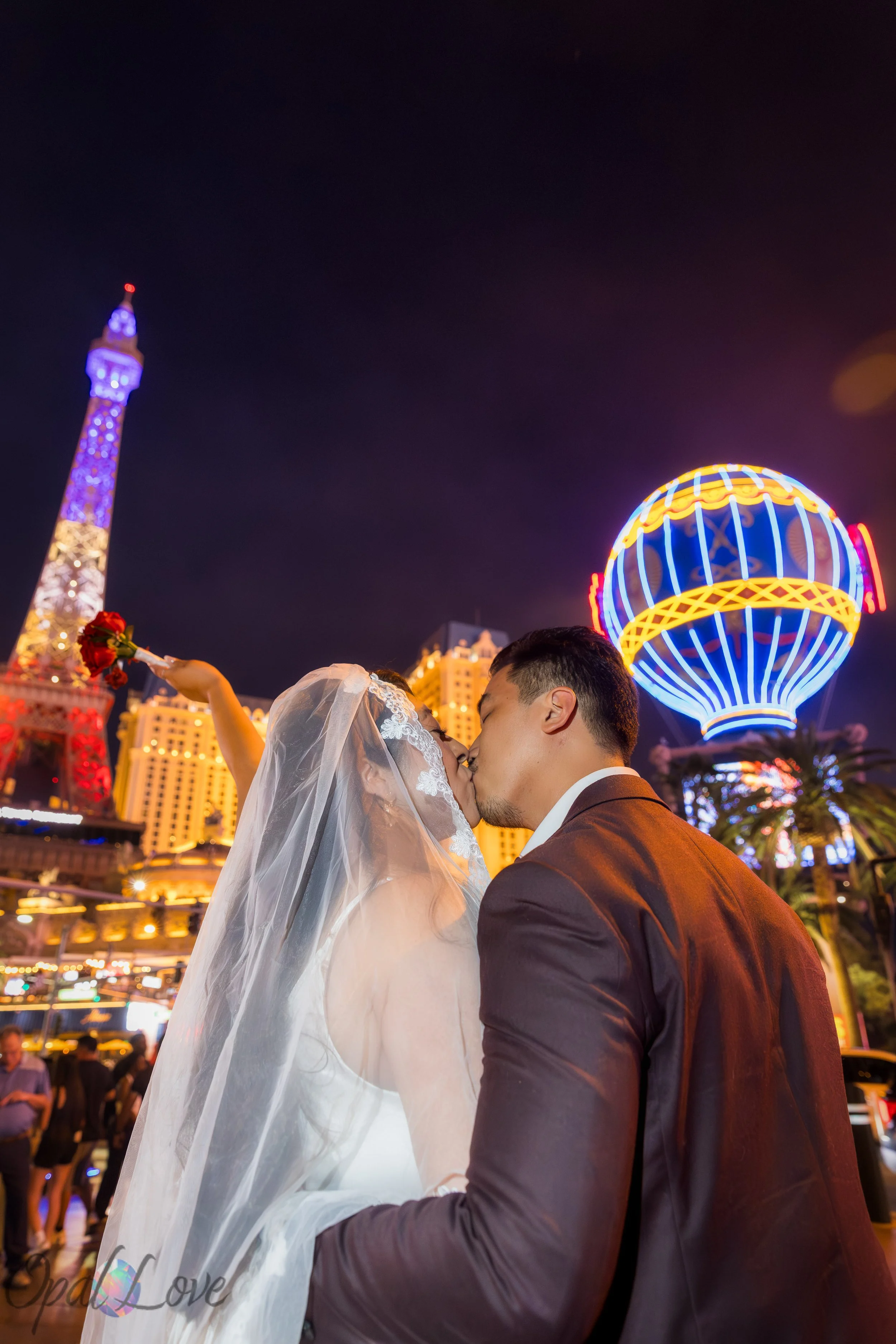 Bride and groom sharing a kiss with the Paris Las Vegas balloon and Eiffel Tower glowing during their nighttime Las Vegas elopement photos.
