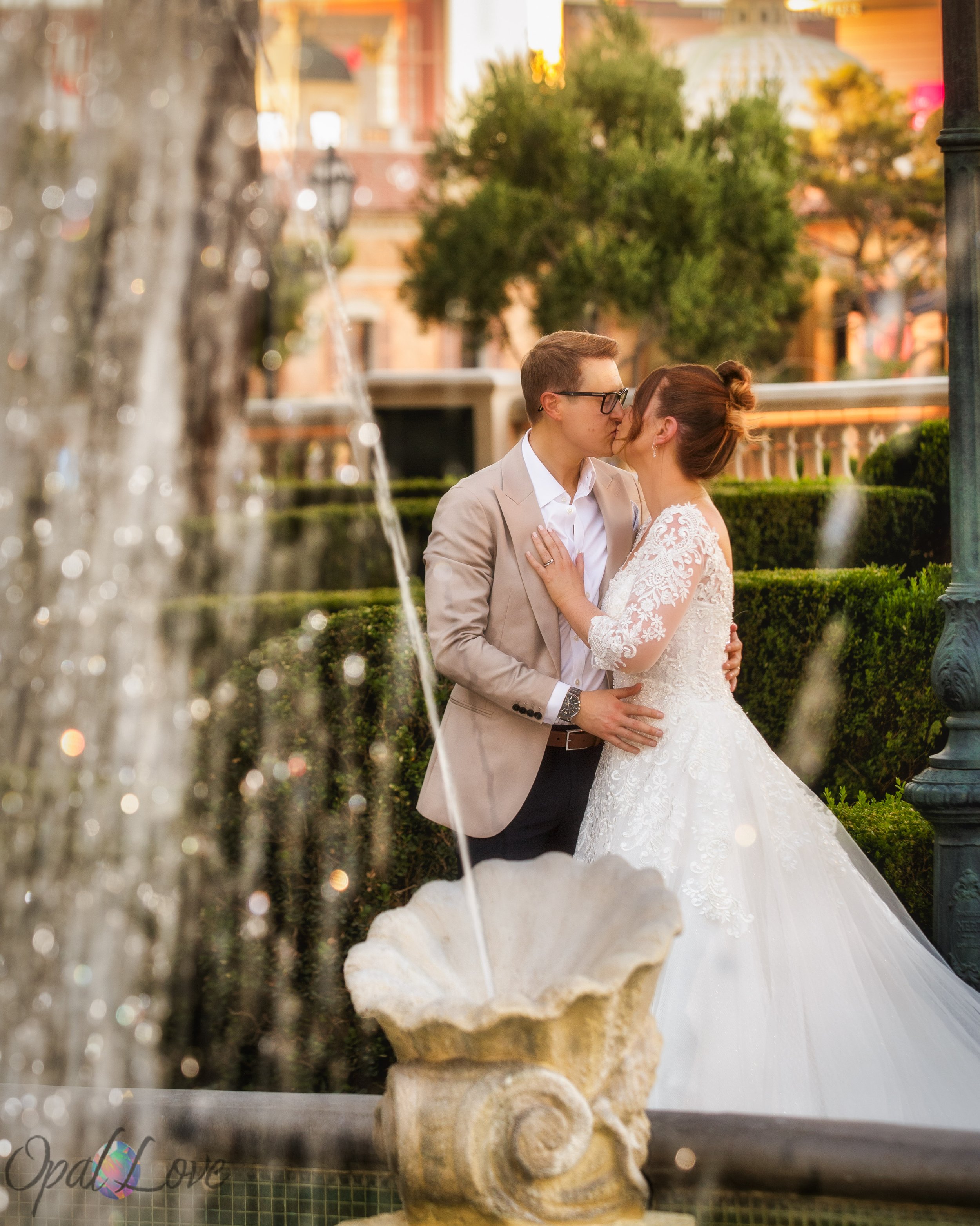 Newlyweds kissing while framed by sparkling fountain streams in a Las Vegas courtyard.