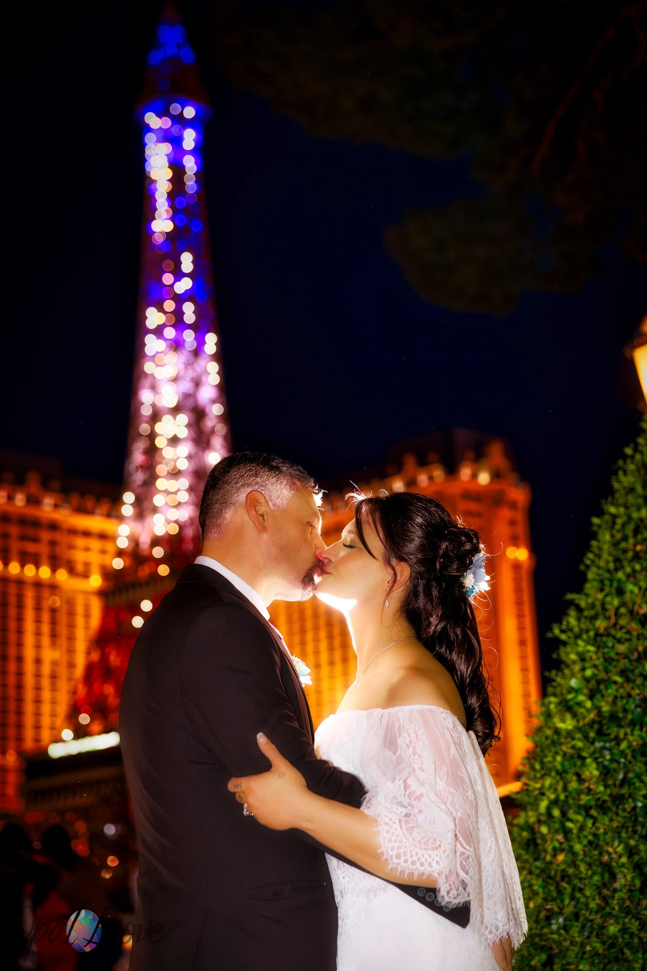 Couple sharing a kiss during a Las Vegas photo tour at the Bellagio, nighttime portraits with Eiffel Tower lights in the background