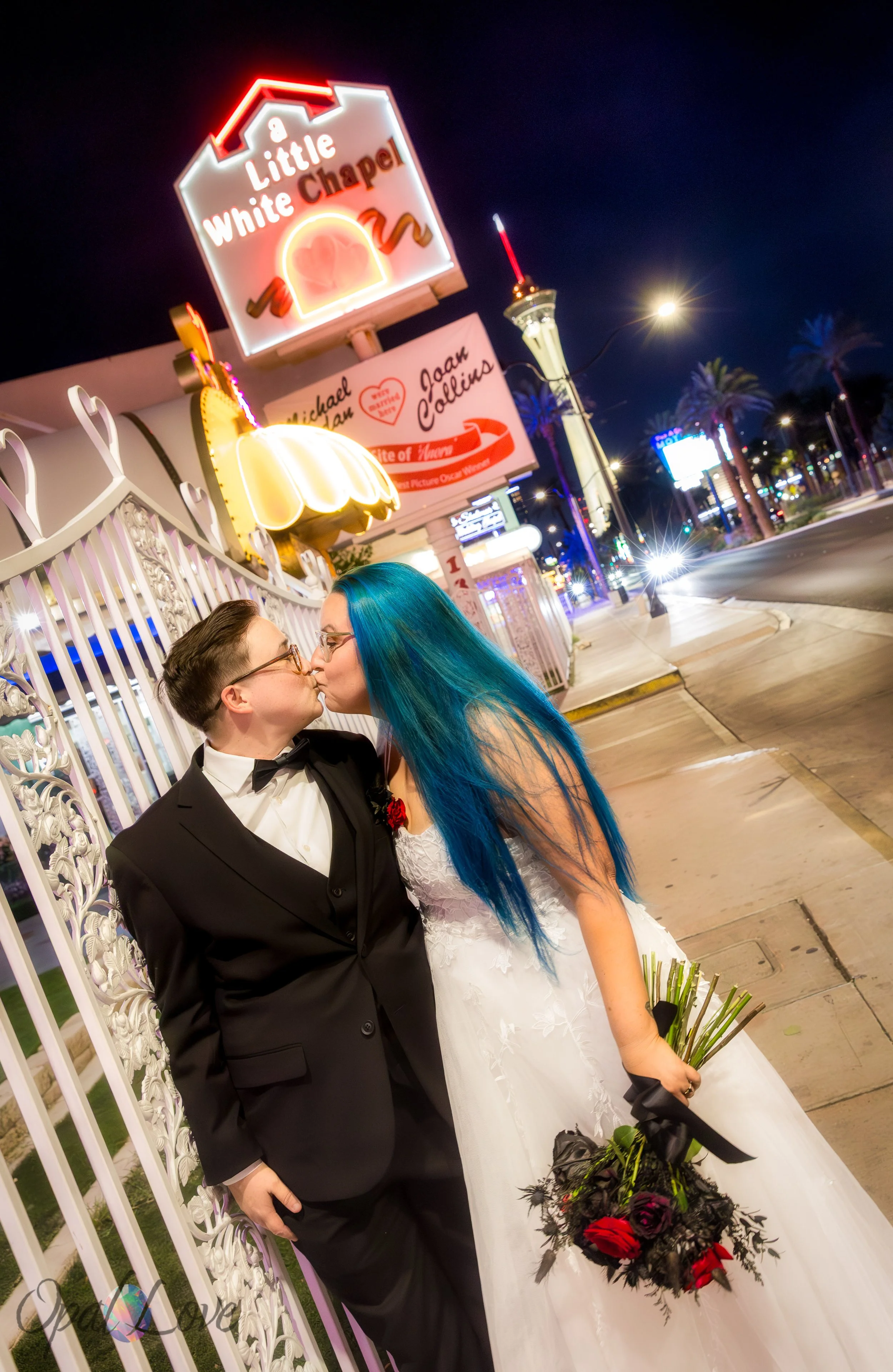 Couple kissing along Las Vegas Boulevard with the chapel sign glowing behind them