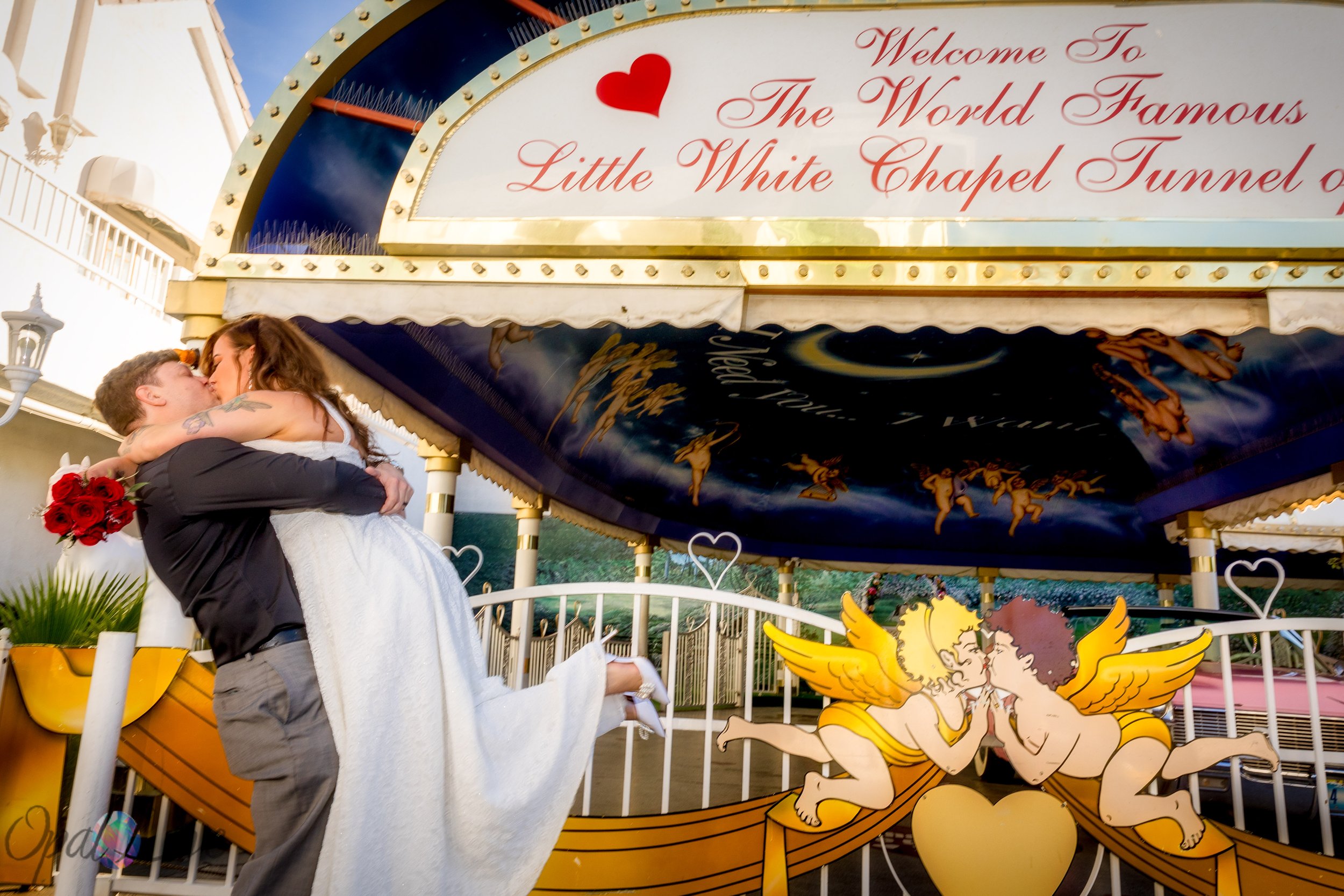 Groom lifting the bride for a kiss beneath the Little White Chapel Tunnel of Love sign.