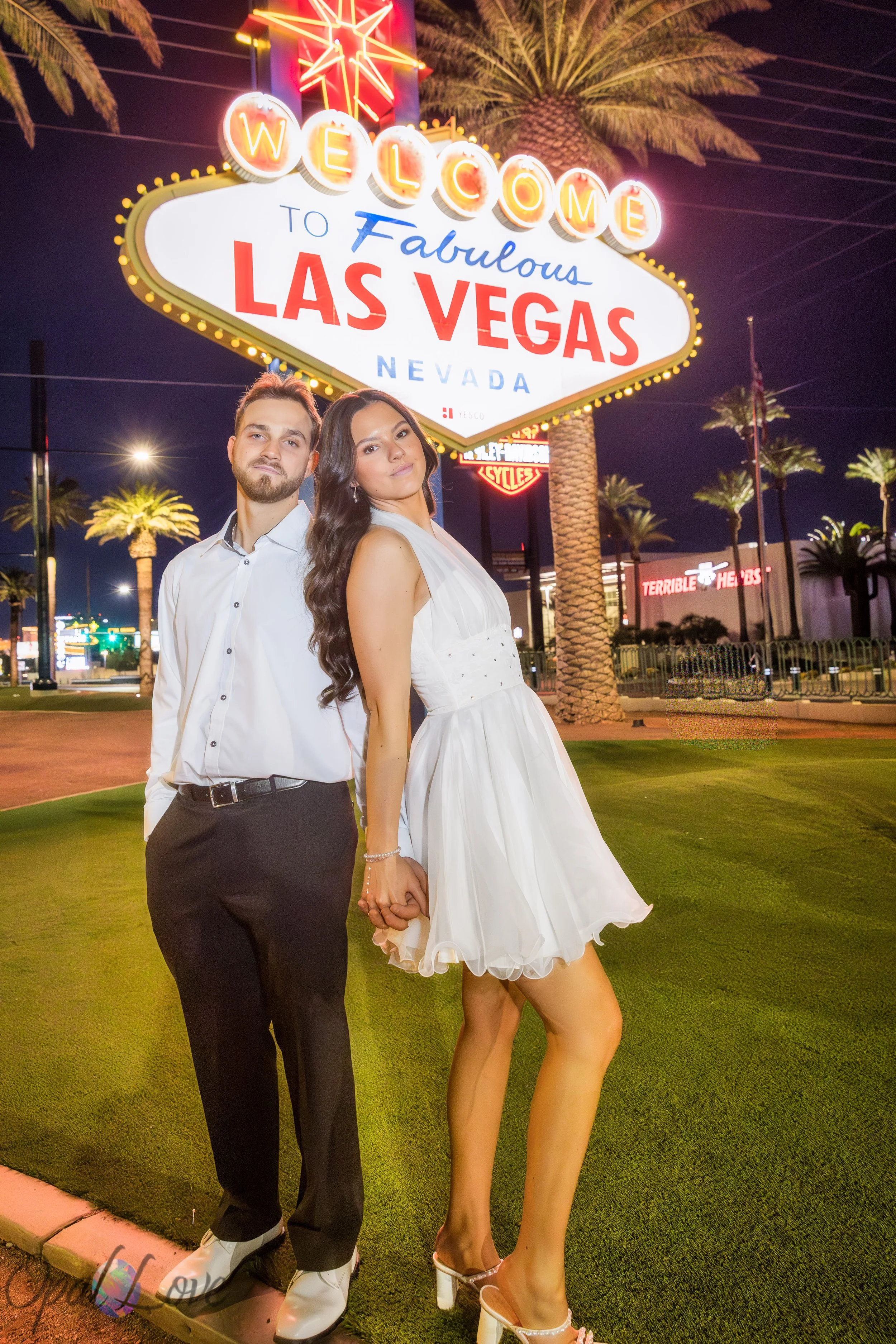 Couple holding hands beneath the illuminated Welcome to Fabulous Las Vegas sign at night.