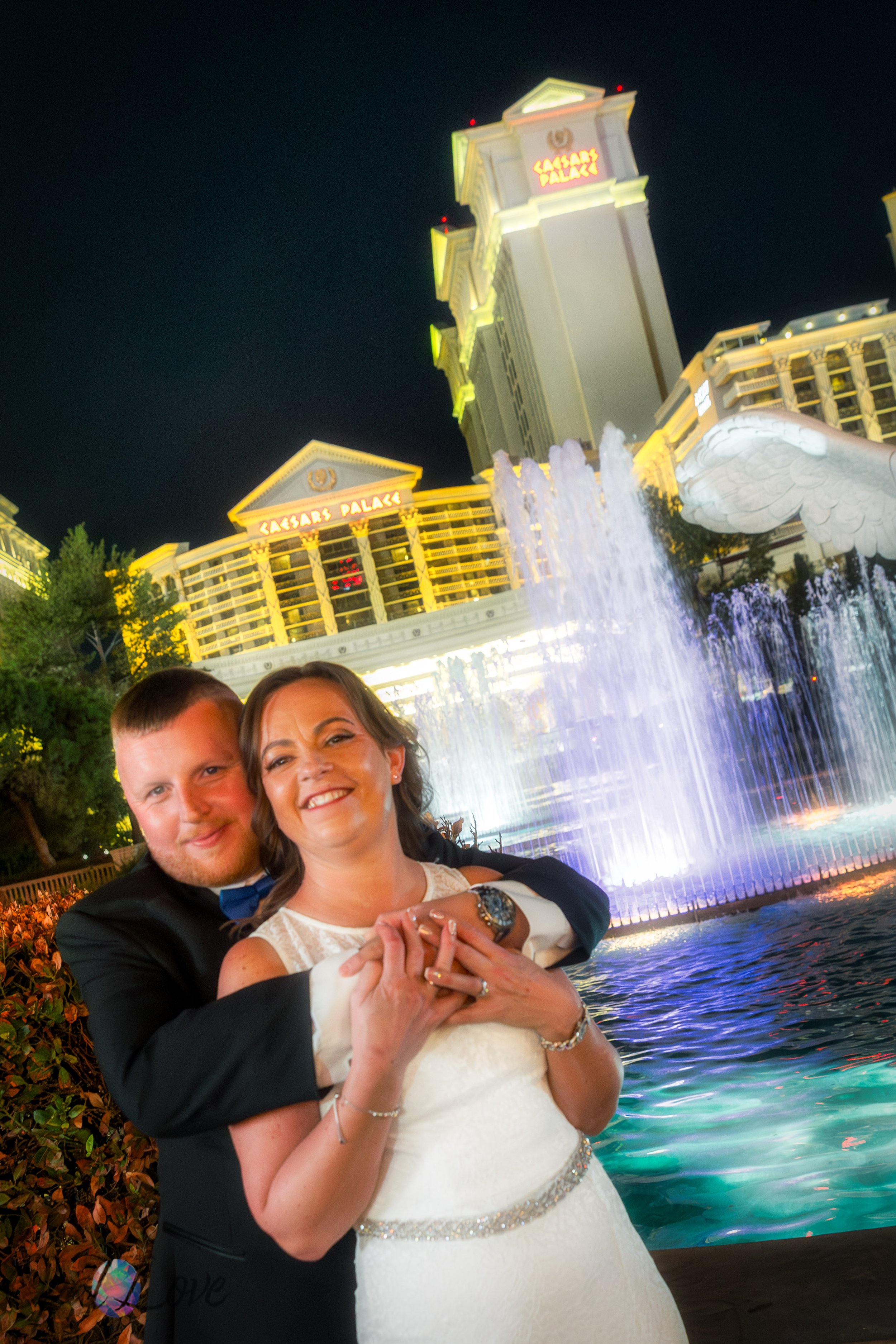 Groom hugging bride in front of the fountains at Caesars Palace during their nighttime photo tour.