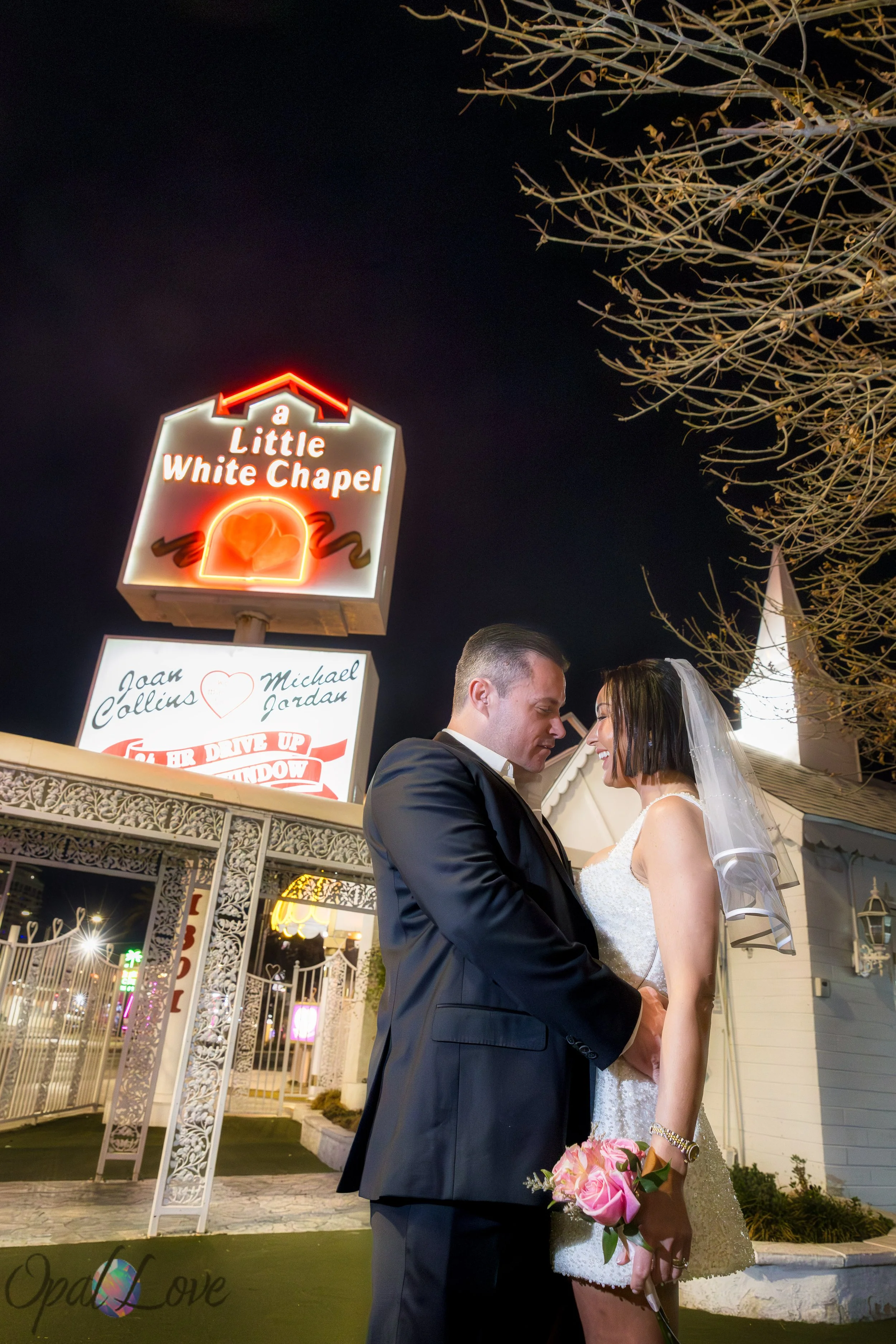 Bride and groom posing under the Little White Wedding Chapel sign at night in Las Vegas.