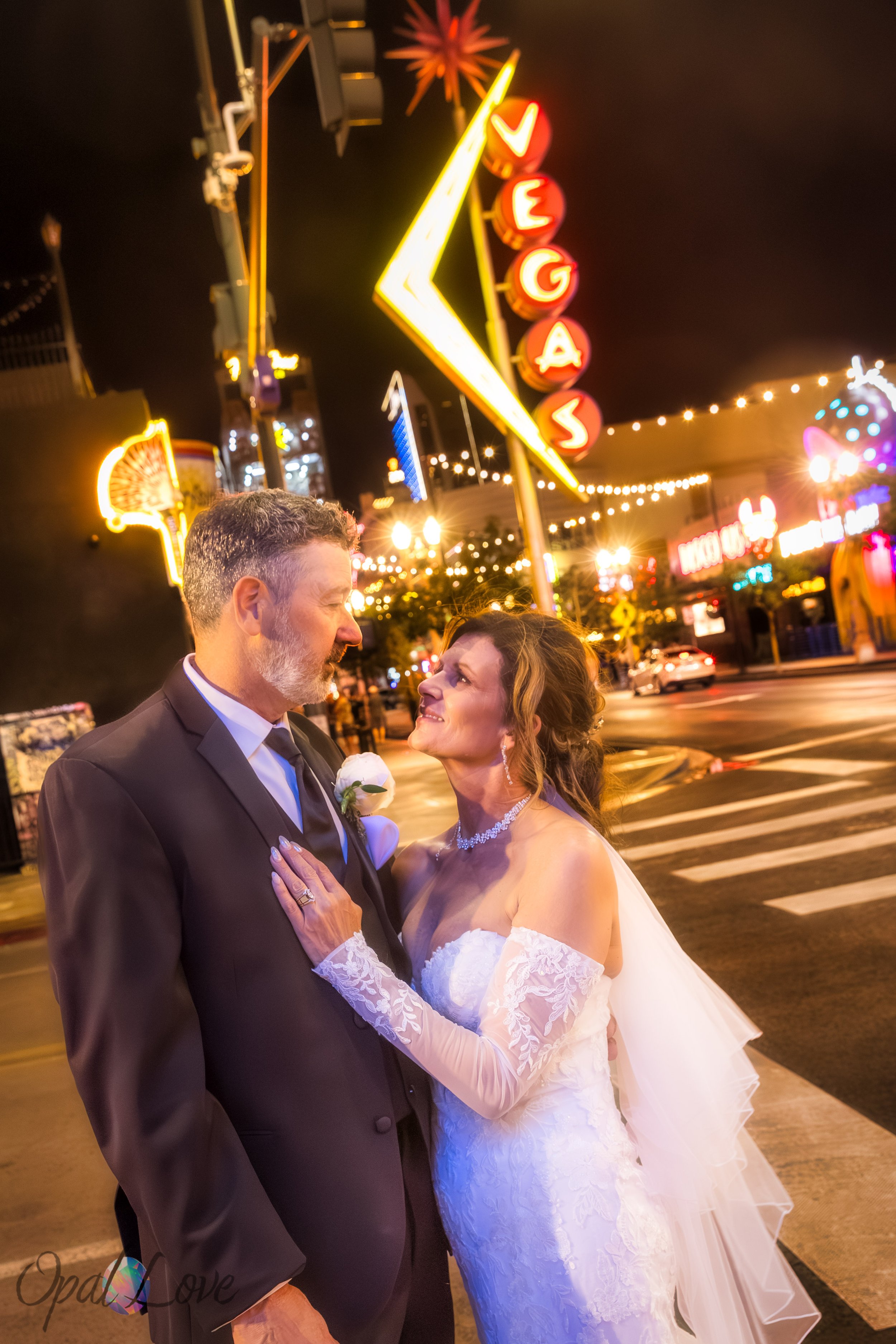 Couple standing under vintage Vegas sign lights, smiling at each other.
