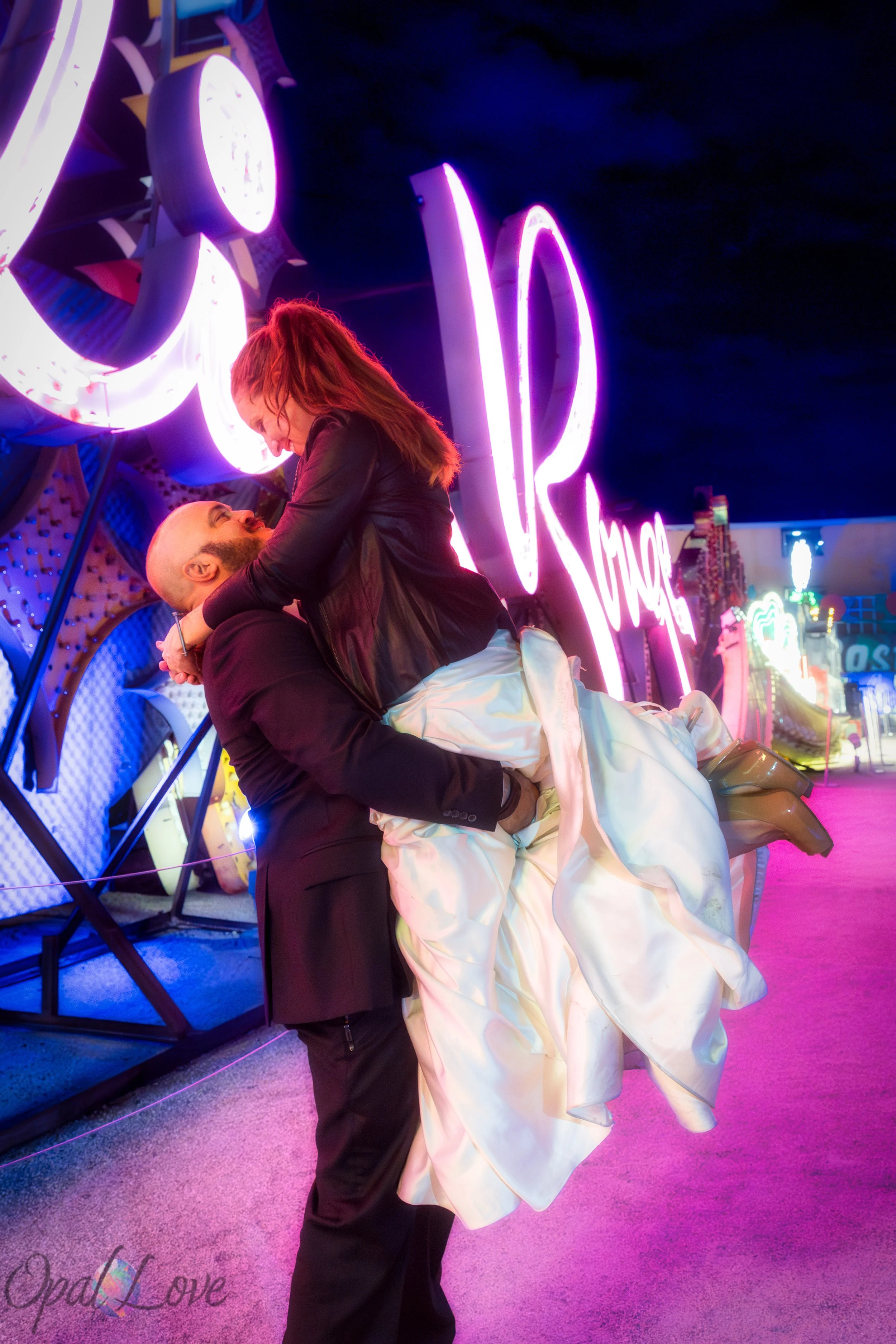 Couple sharing a fun moment surrounded by vintage neon signs at the Neon Boneyard in downtown Las Vegas captured by Opal Love Photography.