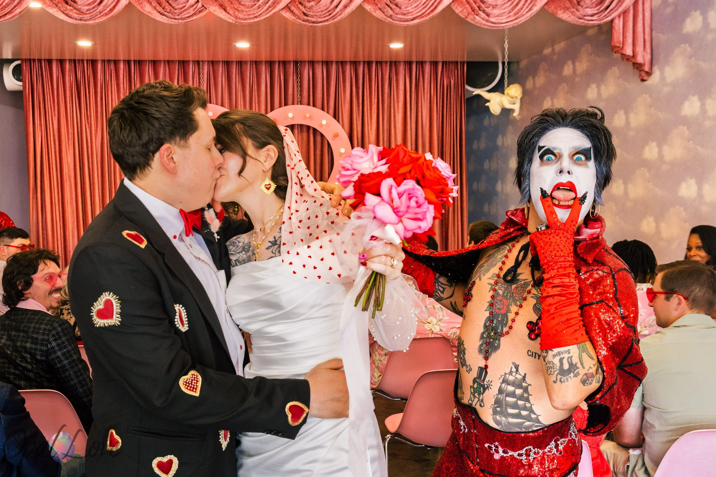 Rachel and Tom kiss during their Las Vegas wedding ceremony as Hellvis reacts beside them at A Sure Thing Wedding Chapel.