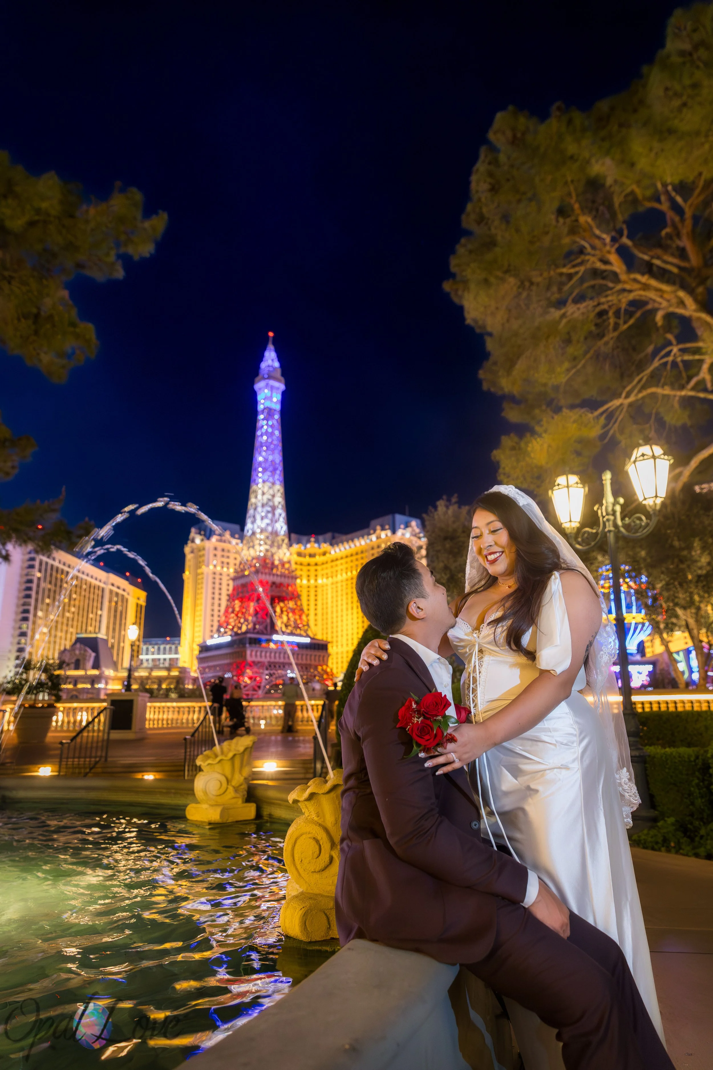 Newly married couple posing beside the Bellagio fountains with the Paris Las Vegas Eiffel Tower glowing in the background during their Las Vegas elopement photo tour.