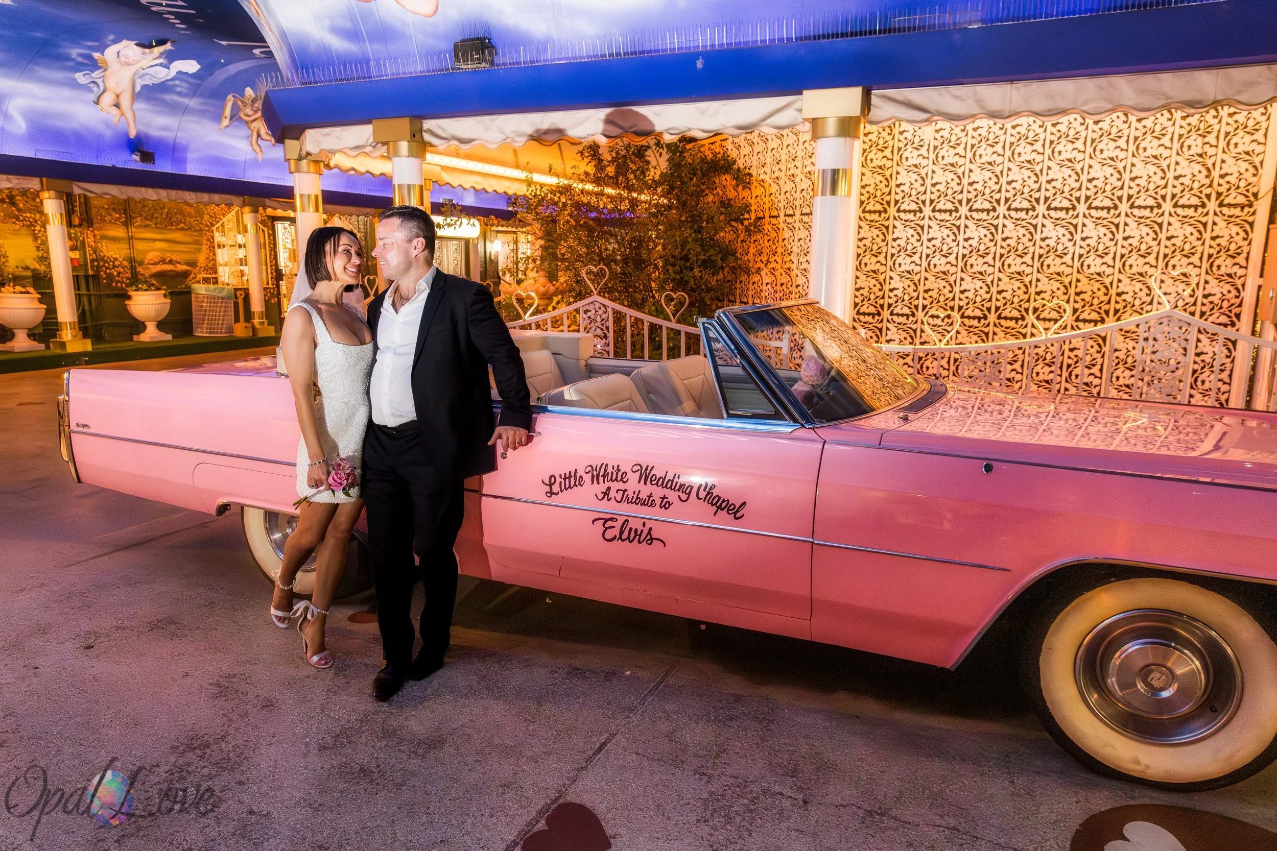 Newlyweds standing beside the vintage pink Cadillac during their Las Vegas elopement photo session.