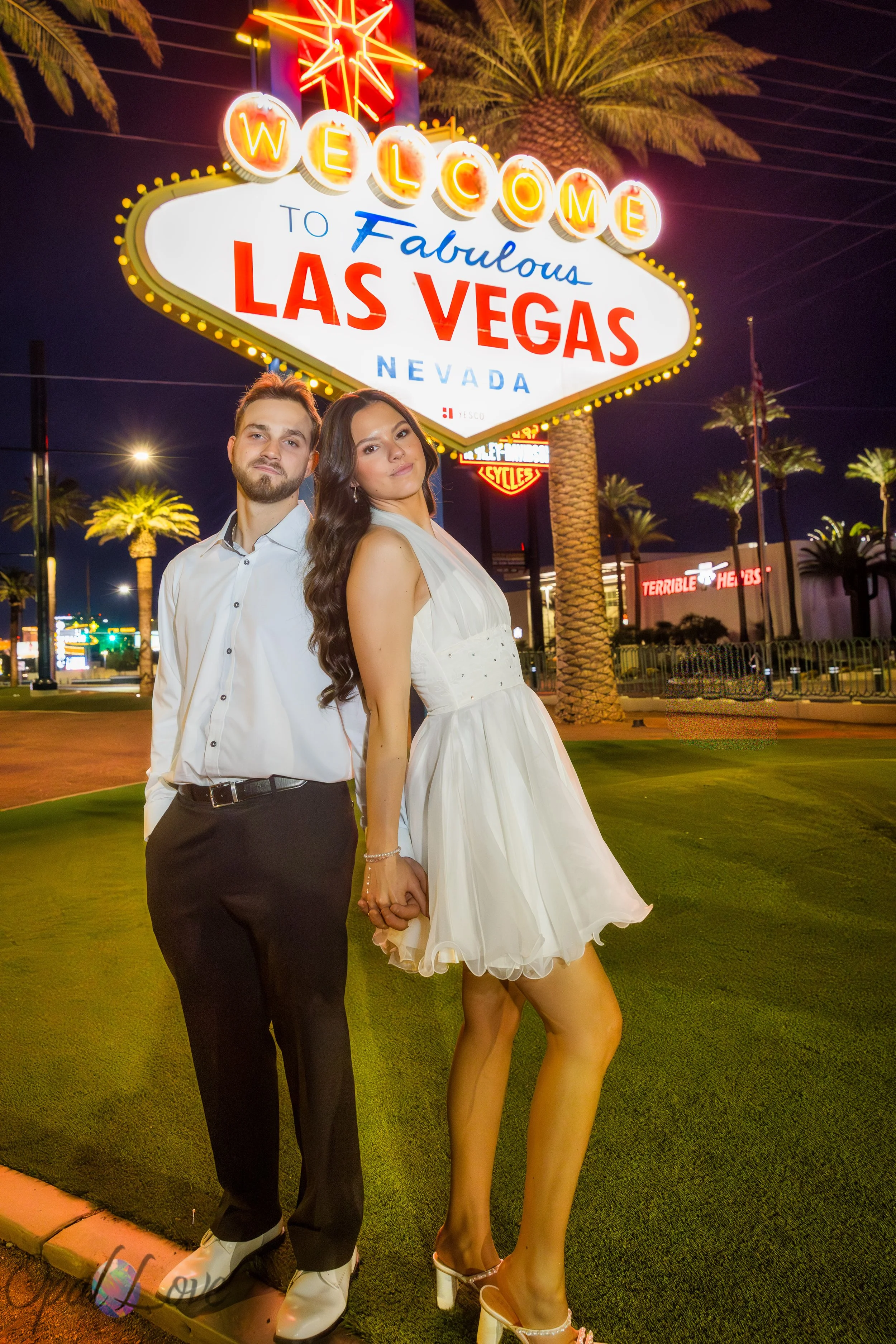 Bride and groom posing playfully beneath the Welcome to Fabulous Las Vegas sign during their evening photo tour.