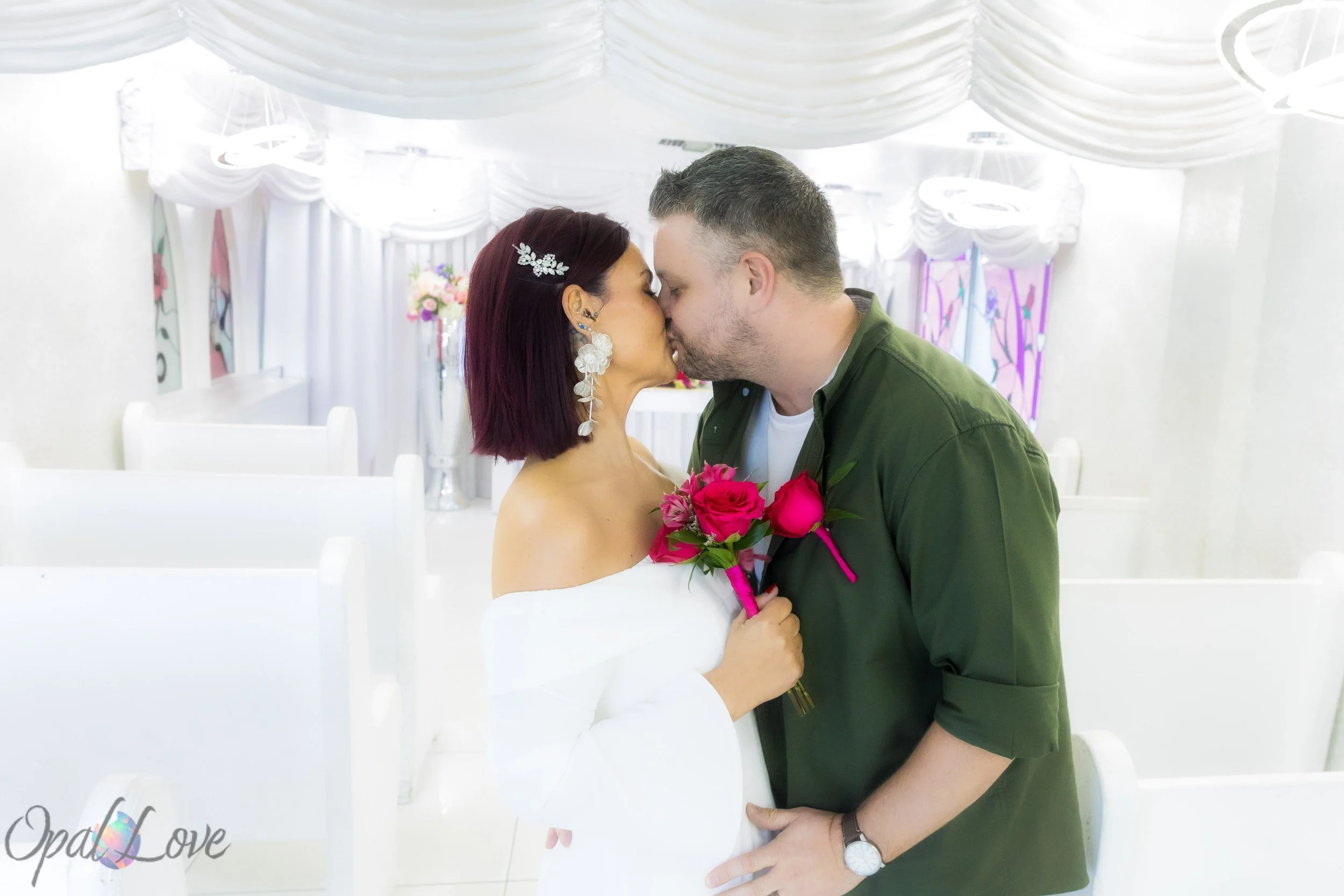 Newly married couple sharing a kiss in the white chapel aisle at A Little White Wedding Chapel.