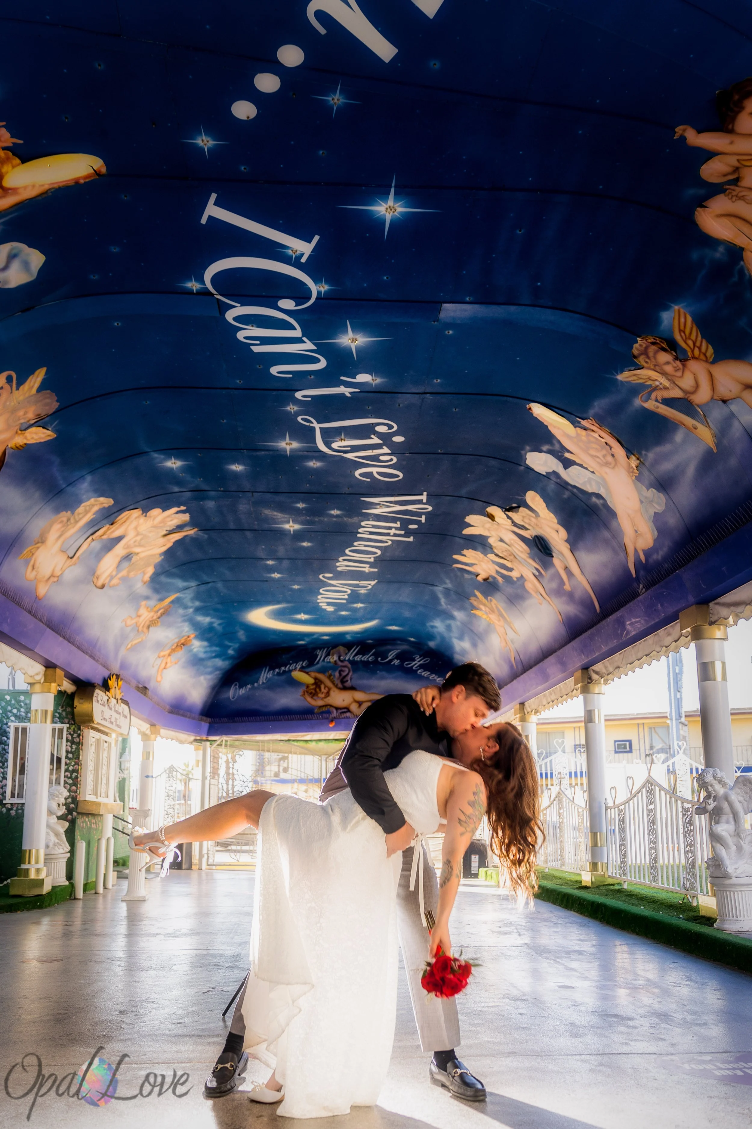 Groom dipping and kissing his bride beneath the painted Tunnel of Love chapel canopy.